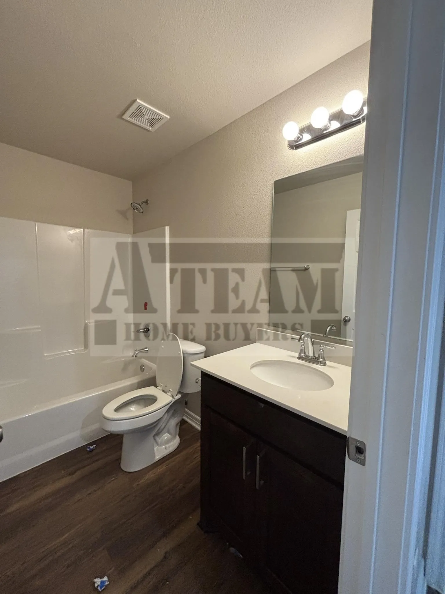Bathroom featuring a dark wood-finish vanity with a white countertop, an oval undermount sink, a three-bulb vanity light fixture, and a white tub-shower combination