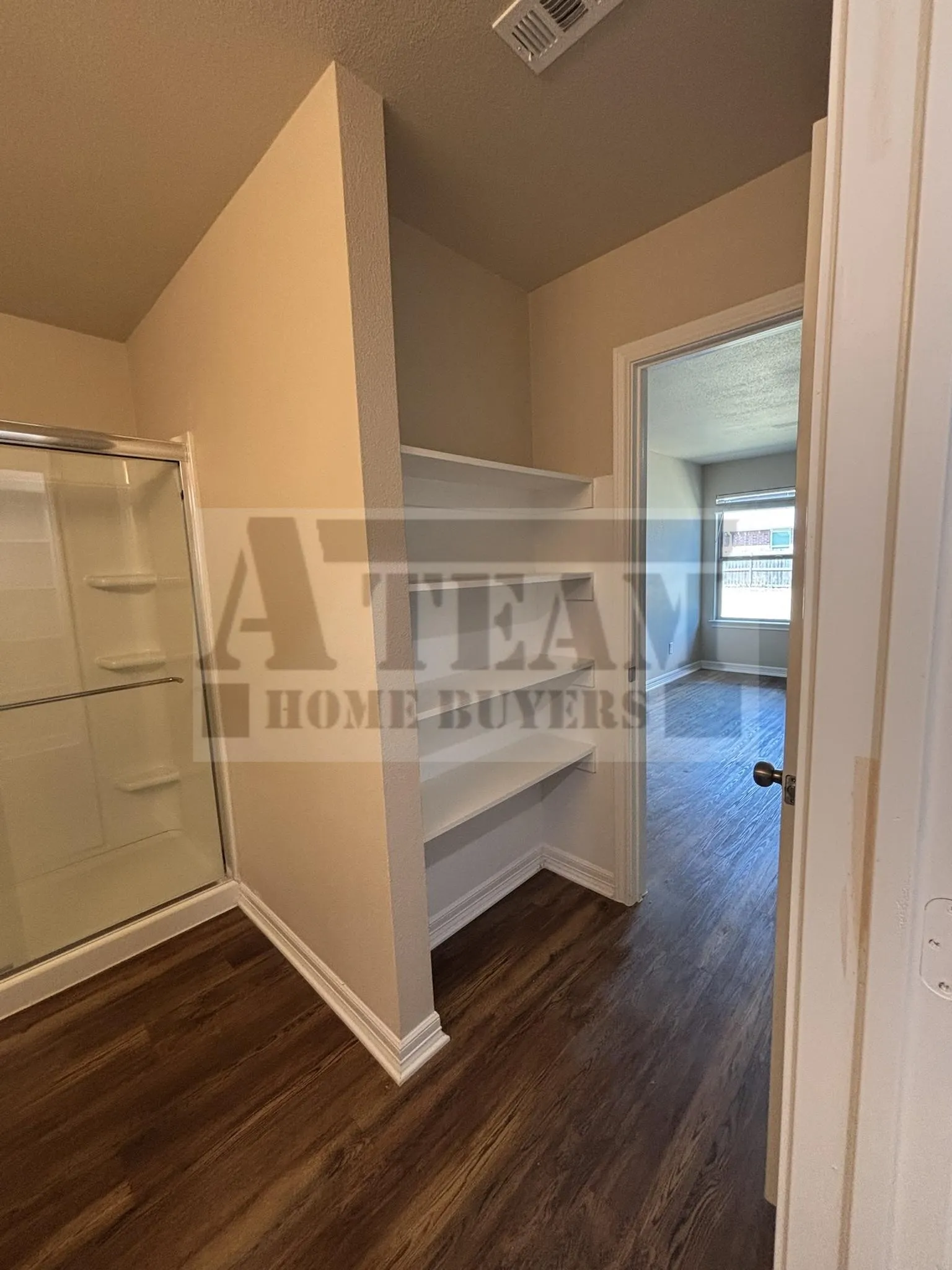 Glass-enclosed shower with white surround, built-in shelving, and wood-finish flooring