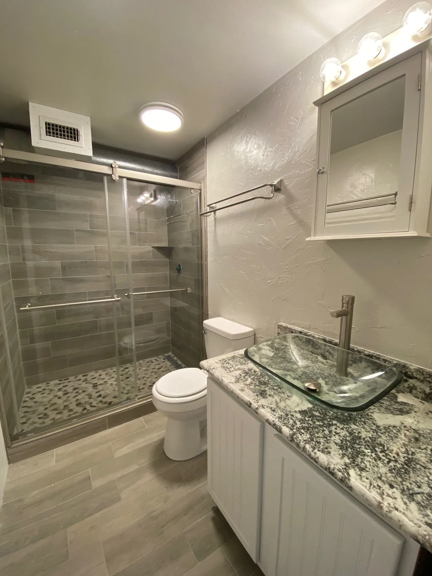 Full bath with a textured wall, vanity, a shower stall, and wood finish floors