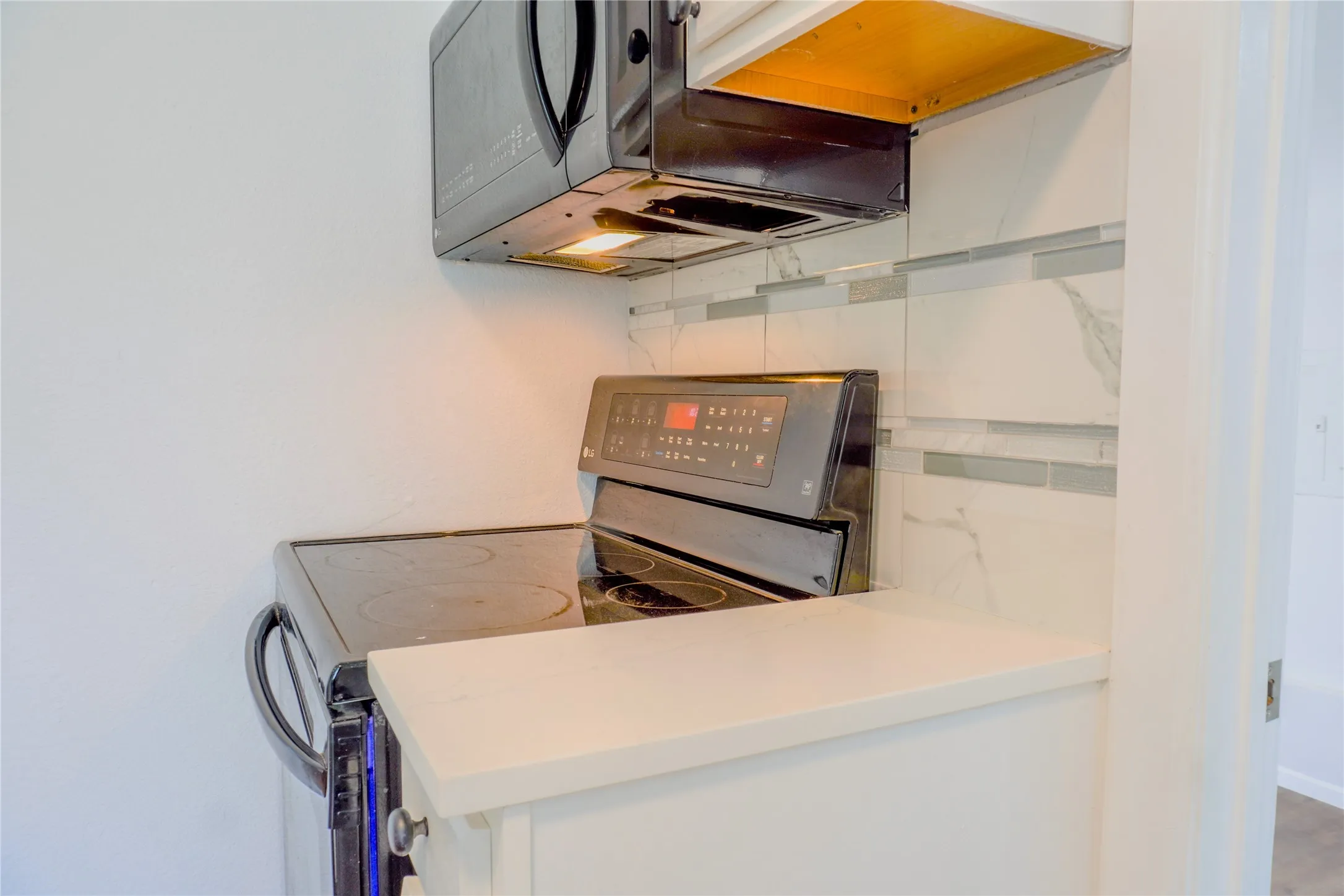 Kitchen featuring a smooth-top electric range, over-the-range microwave, quartz countertop, and a decorative tile backsplash with marble-patterned and glass accents