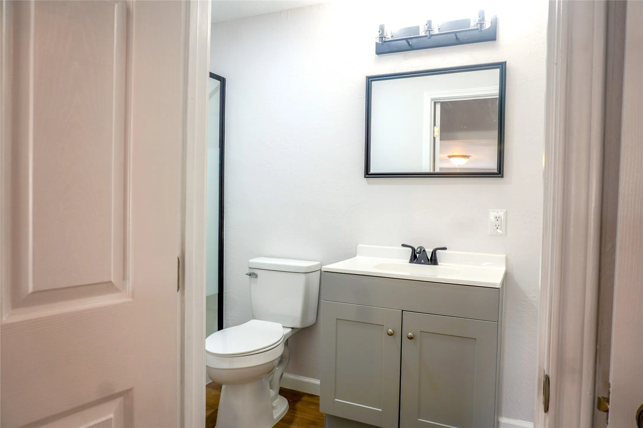 Grey shaker-style vanity with white countertop, integrated sink, matte black faucet, framed vanity mirror, and linear vanity lighting