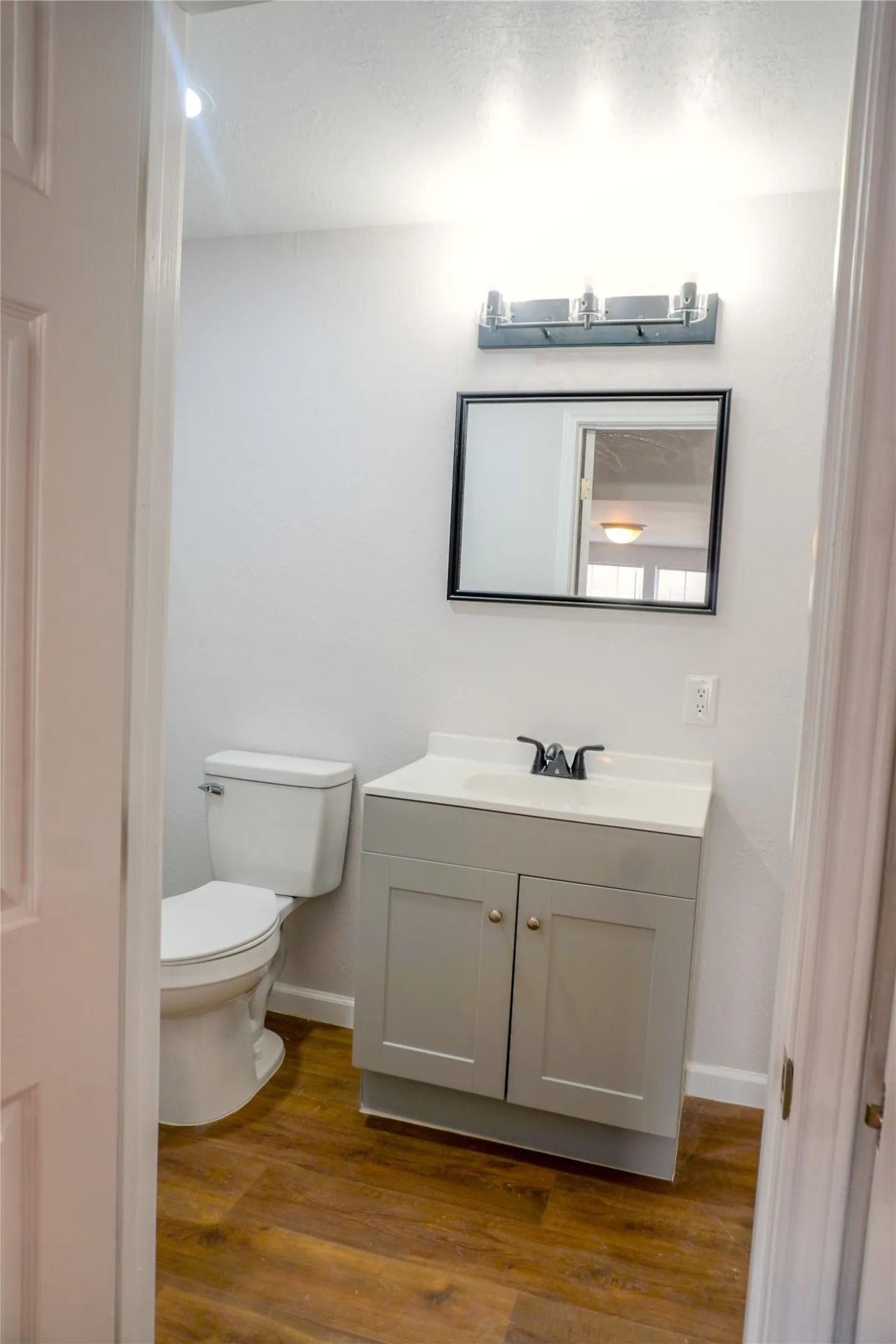 Neutral-toned vanity with an integrated countertop, dark hardware, wall-mounted rectangular mirror, and wood-finish flooring