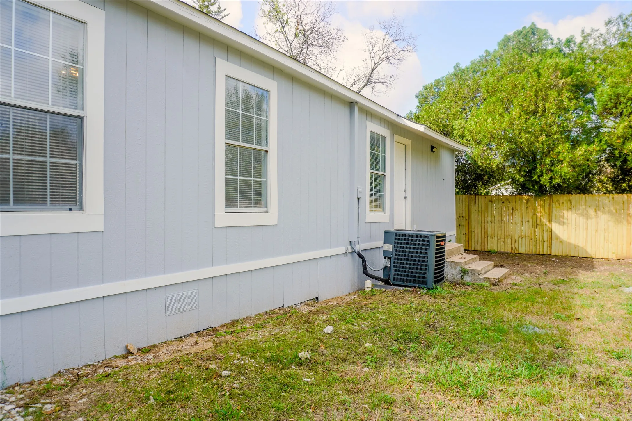 Exterior featuring vertical siding, grid-patterned windows, concrete steps, and a perimeter wood-slat fence