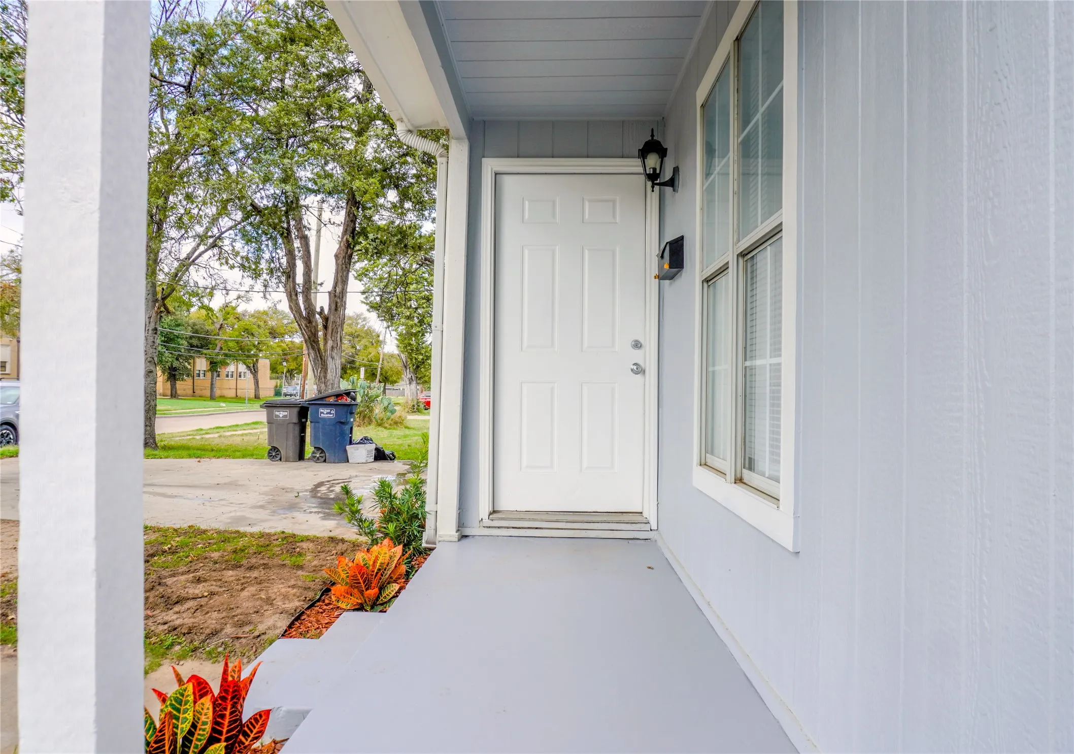 Covered front porch featuring vertical board-and-batten siding, a six-panel entry door, and an exterior wall-mounted lantern light fixture