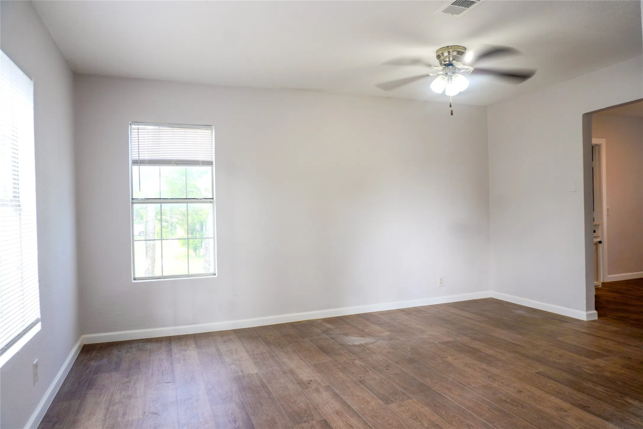 Neutral wall finishes, wood-finish flooring, and a ceiling-mounted light fixture with a fan