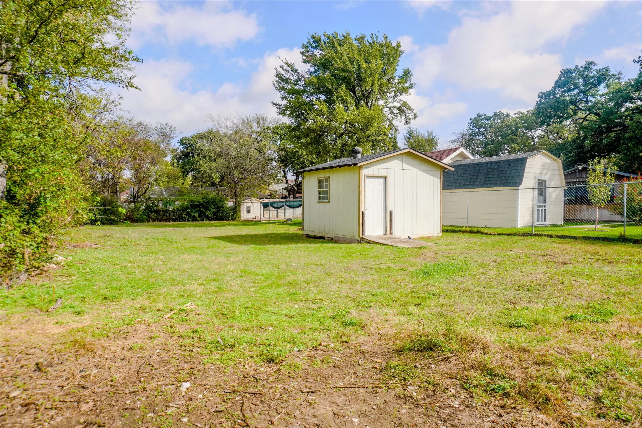 Expansive backyard featuring two detached storage structures, chain-link fencing, and mature trees
