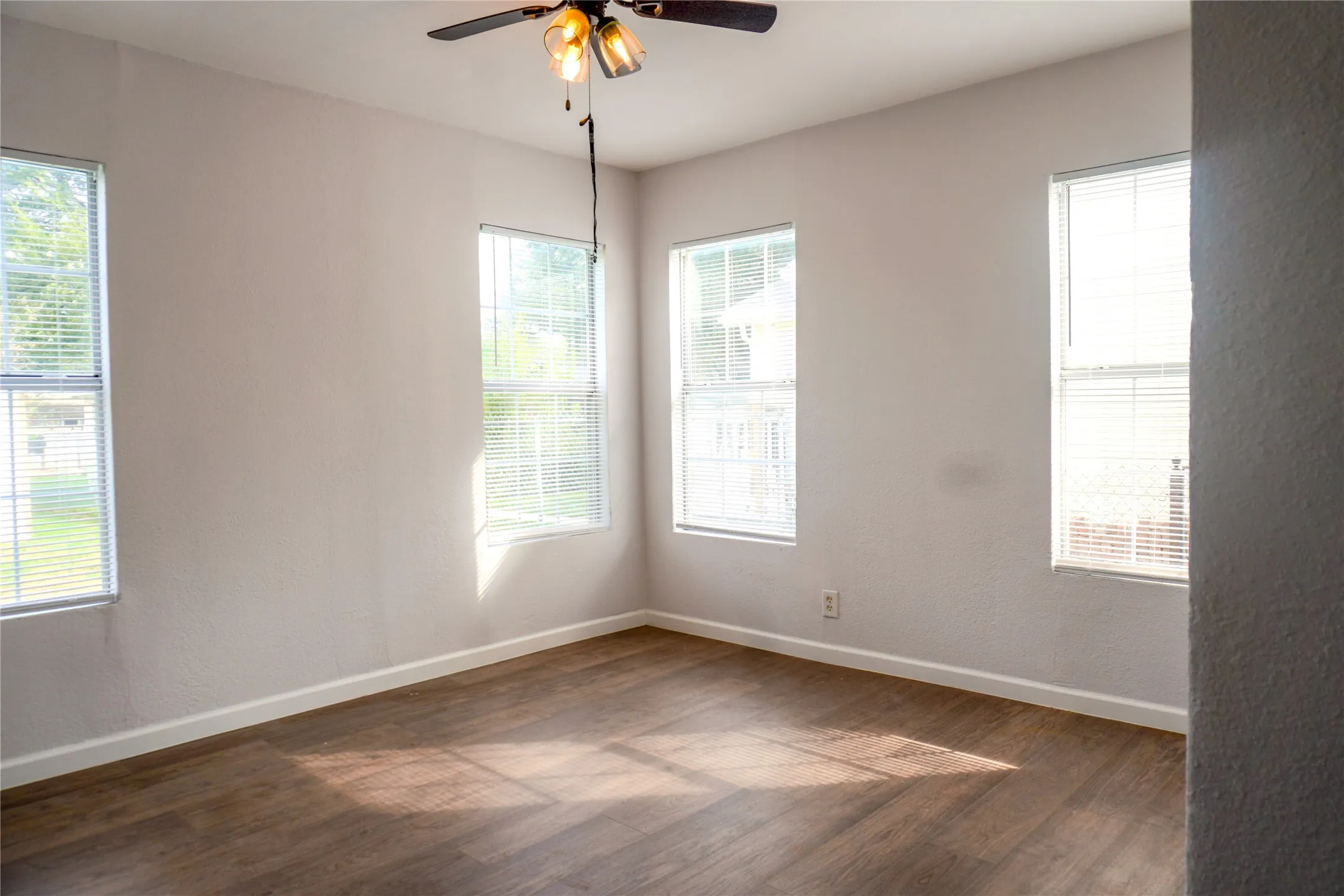 Interior space featuring wood-finish flooring, neutral wall paint, multiple windows with blinds, and a ceiling fan with integrated lighting