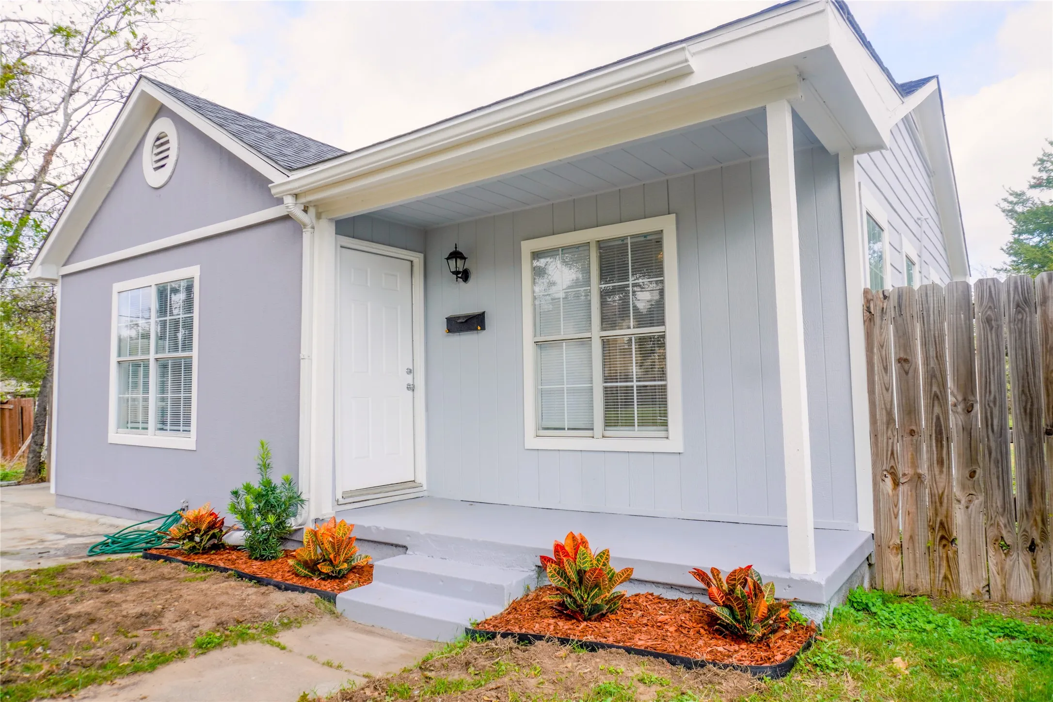 Exterior featuring vertical siding, a covered front porch, multi-pane windows, and a wood-paneled privacy fence