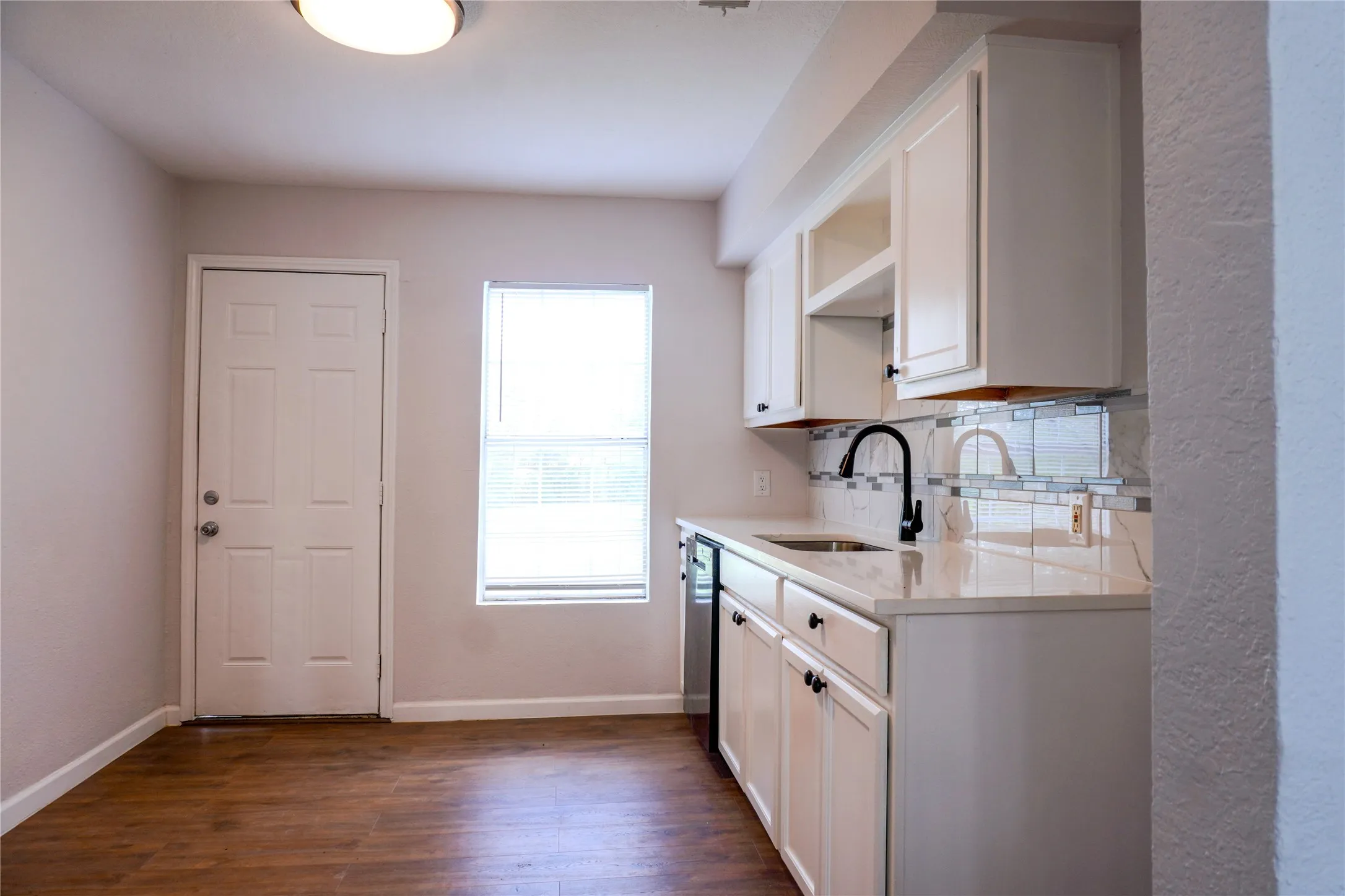 Kitchen featuring white cabinetry, light-toned countertops, tile backsplash, wood-finish flooring, and a matte black gooseneck faucet
