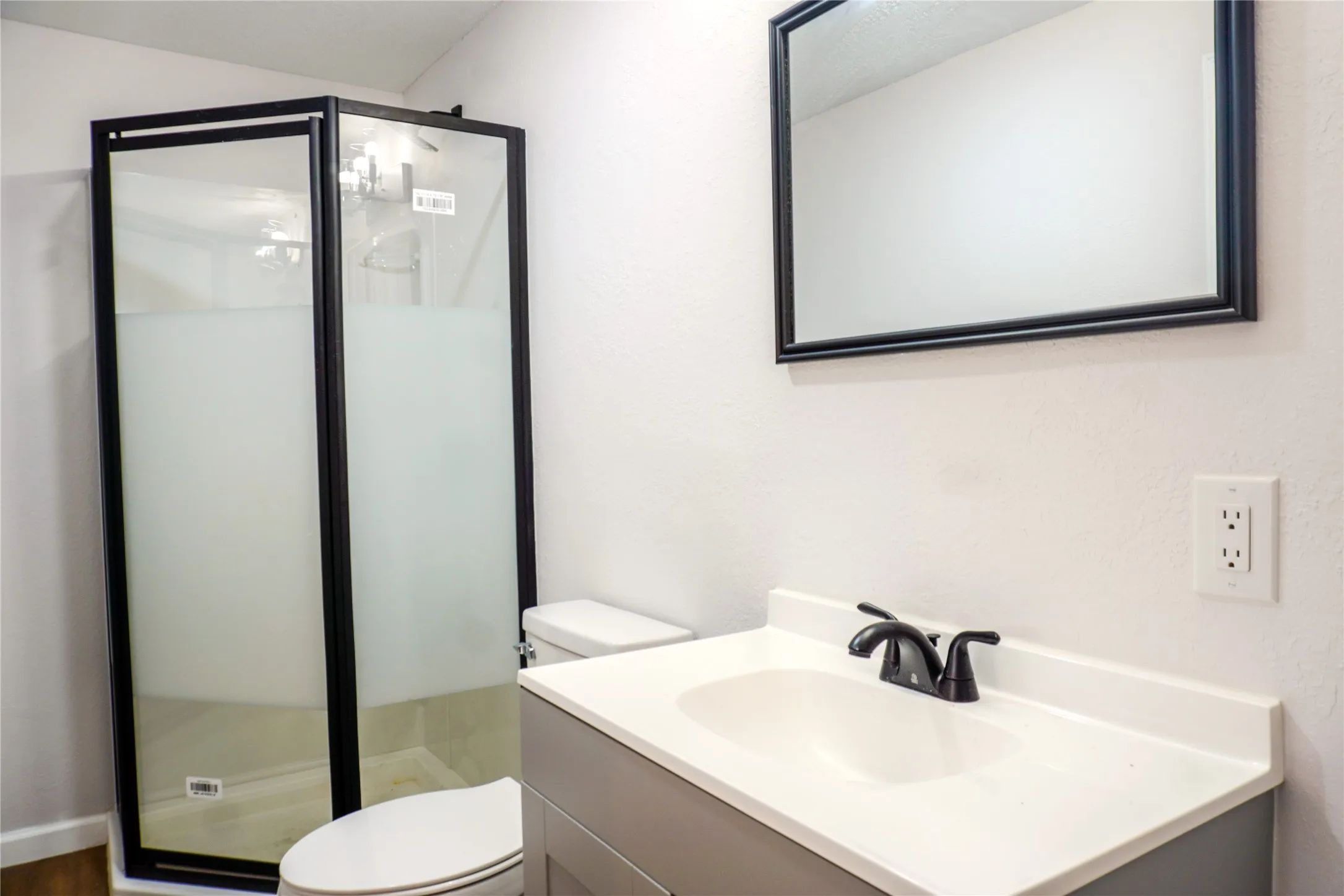 Corner shower enclosure with matte black frame and frosted glass, vanity with integrated basin, matte black faucet, and rectangular wall mirror with a matching black frame
