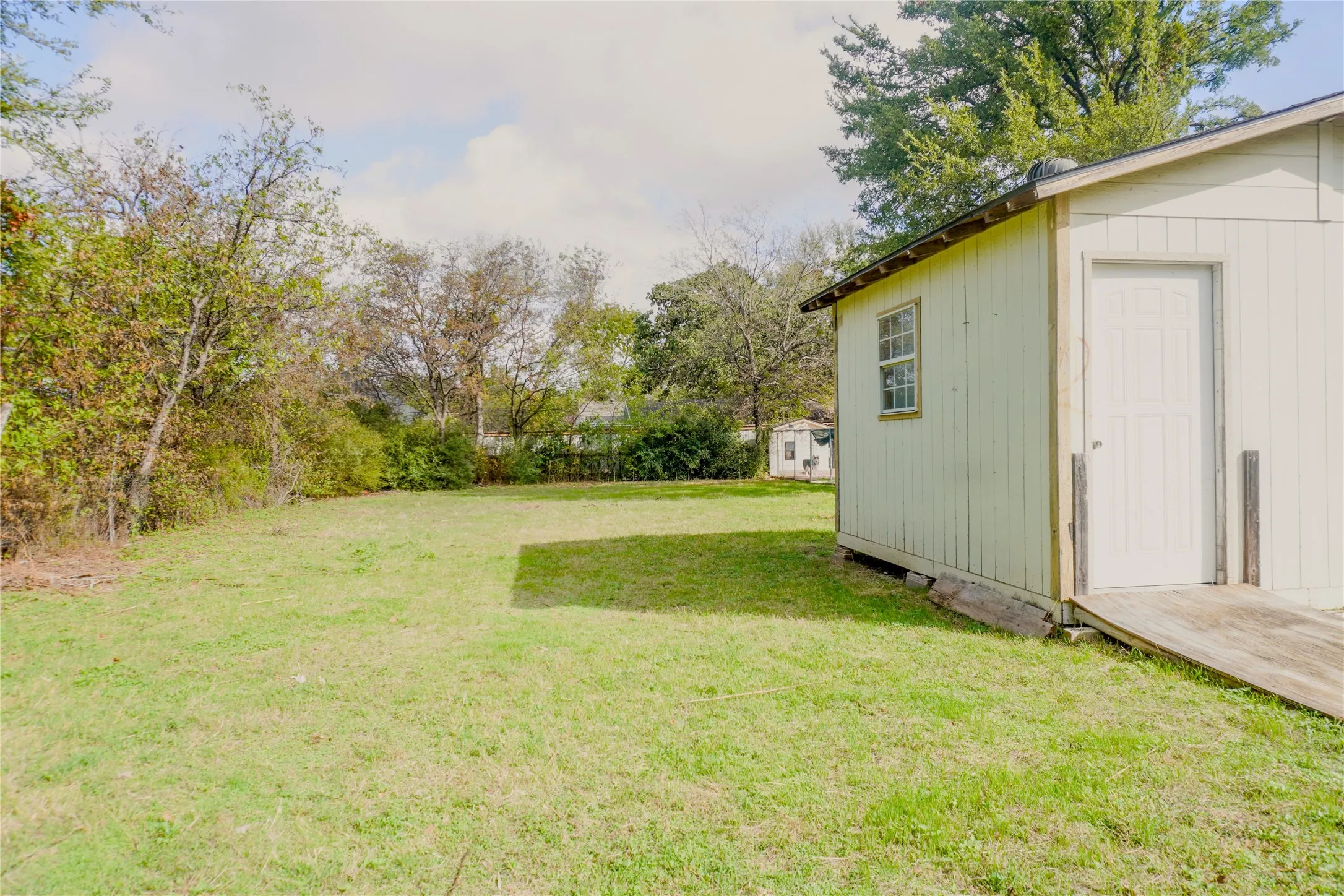 Expansive backyard featuring mature trees, perimeter vegetation, and a detached outbuilding with a wooden ramp entrance