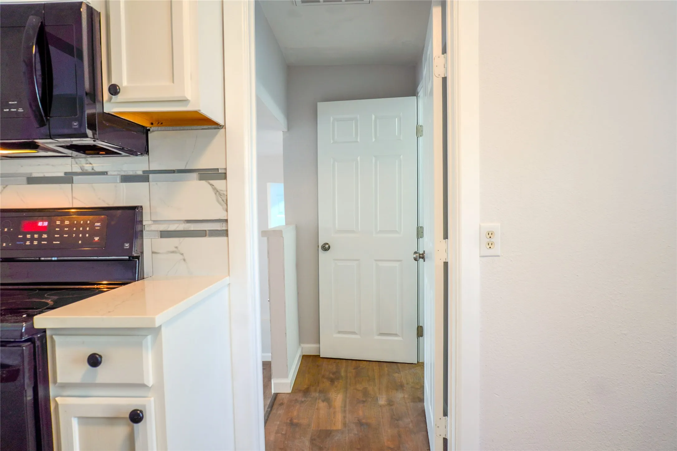 Kitchen featuring white cabinetry, solid-surface countertops, stone-finish tile backsplash, black built-in microwave and range, and wood-finish flooring