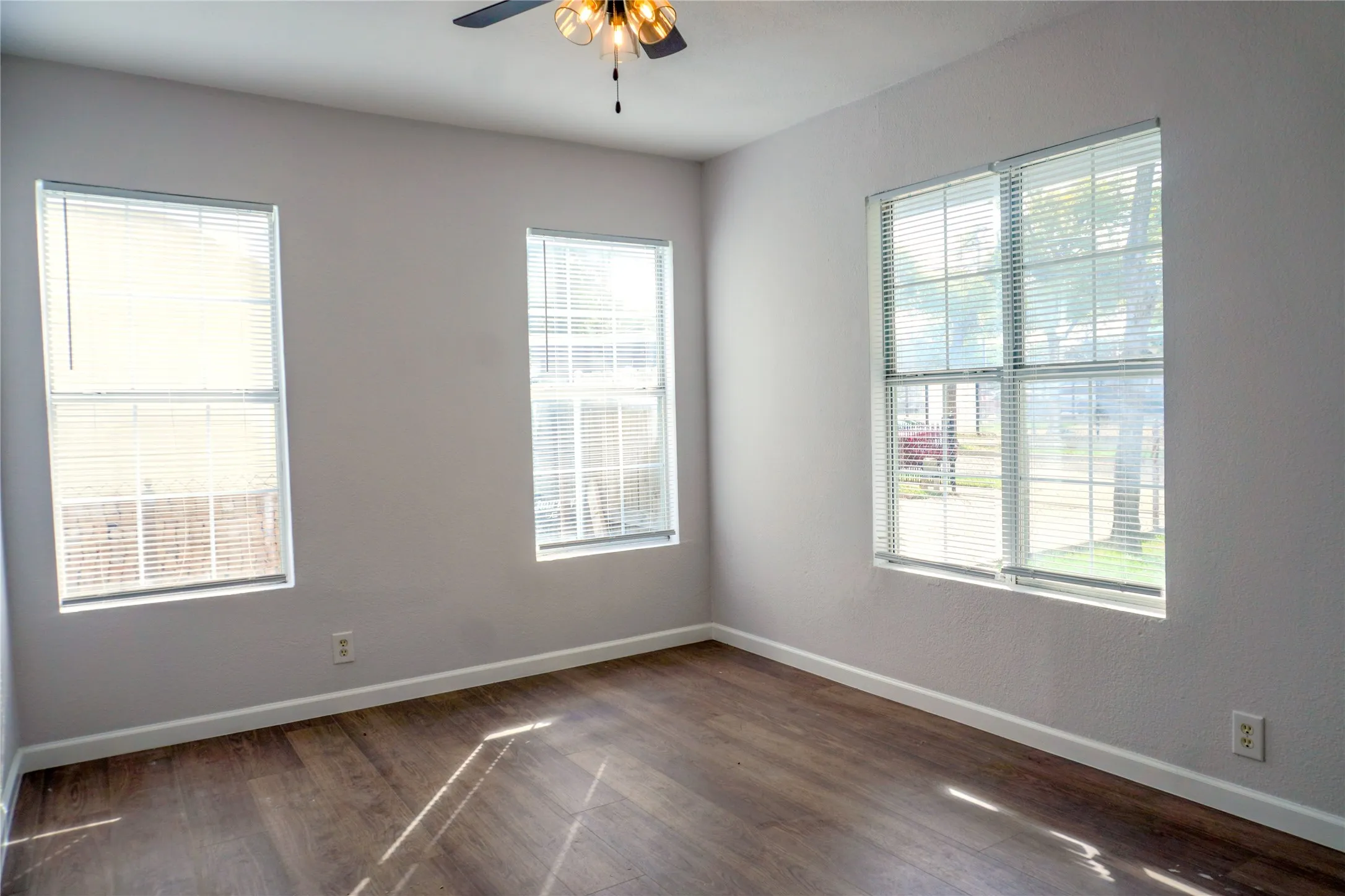 Neutral-toned interior featuring wood-finish flooring, three windows with integrated blinds, and a ceiling-mounted light fixture