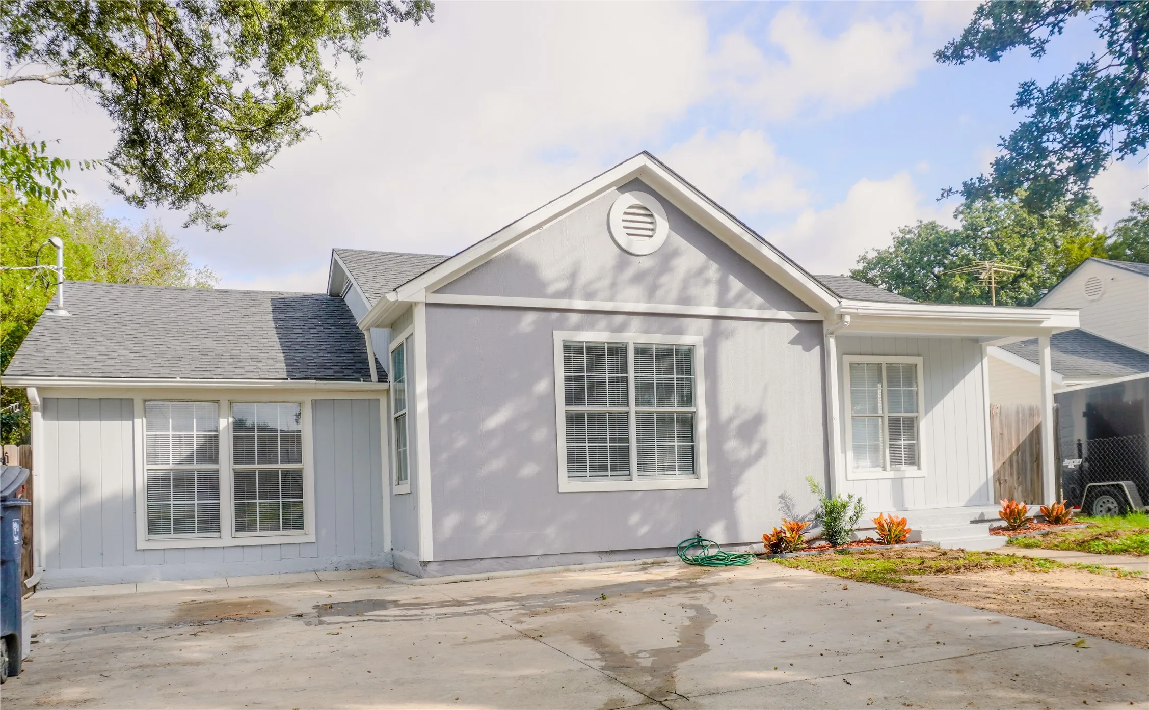 Single-story residence featuring a light gray exterior, vertical siding, gabled roofline, concrete driveway, and covered front entry