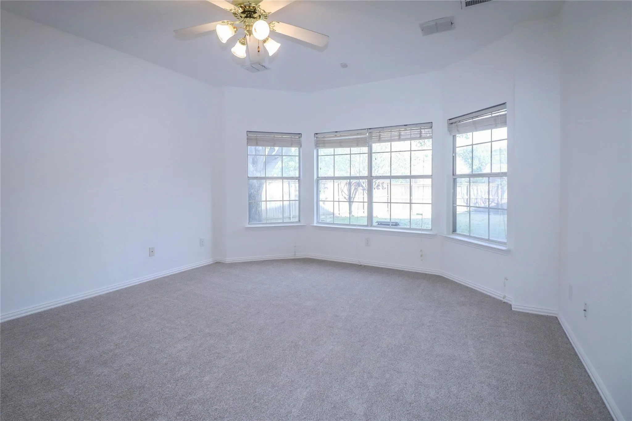 Neutral-toned wall-to-wall carpeting, bay window configuration, multi-pane windows with fitted blinds, and a ceiling-mounted lighting fixture with an integrated fan