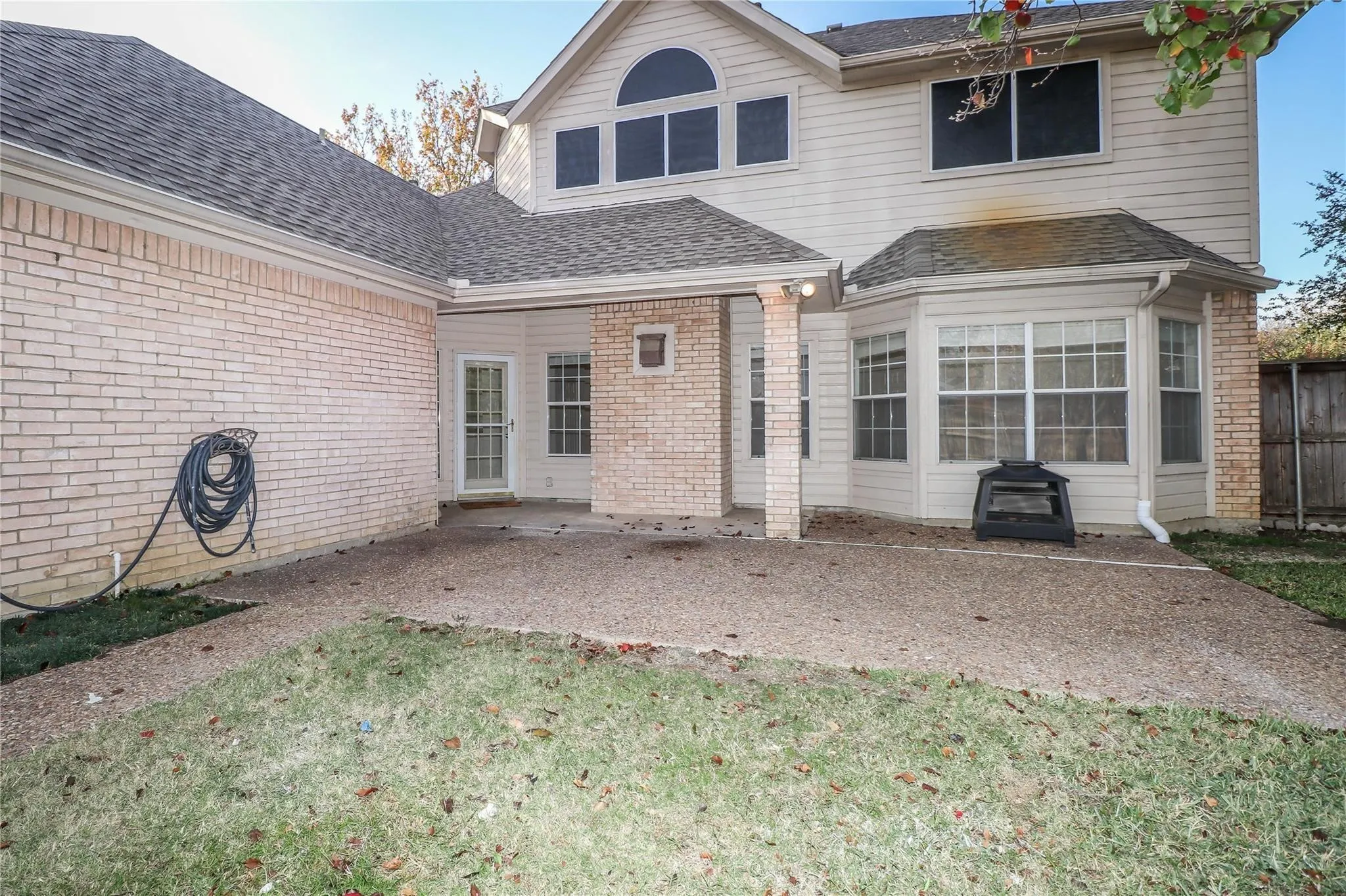Rear exterior featuring light-toned brick masonry, a covered concrete patio, multi-pane windows, and a combination of shingle roofing and horizontal siding