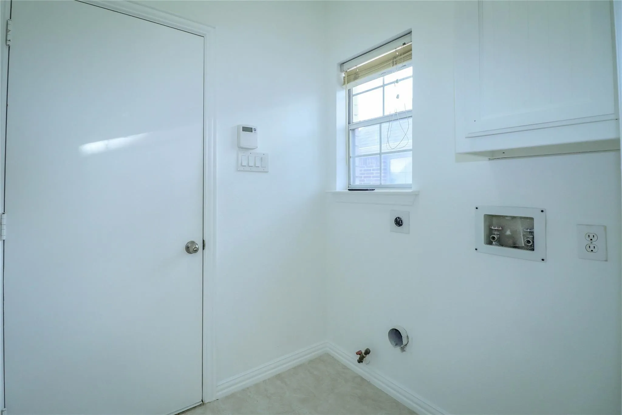 Utility area featuring a wall-mounted upper cabinet, a window with horizontal blinds, and dedicated plumbing connections