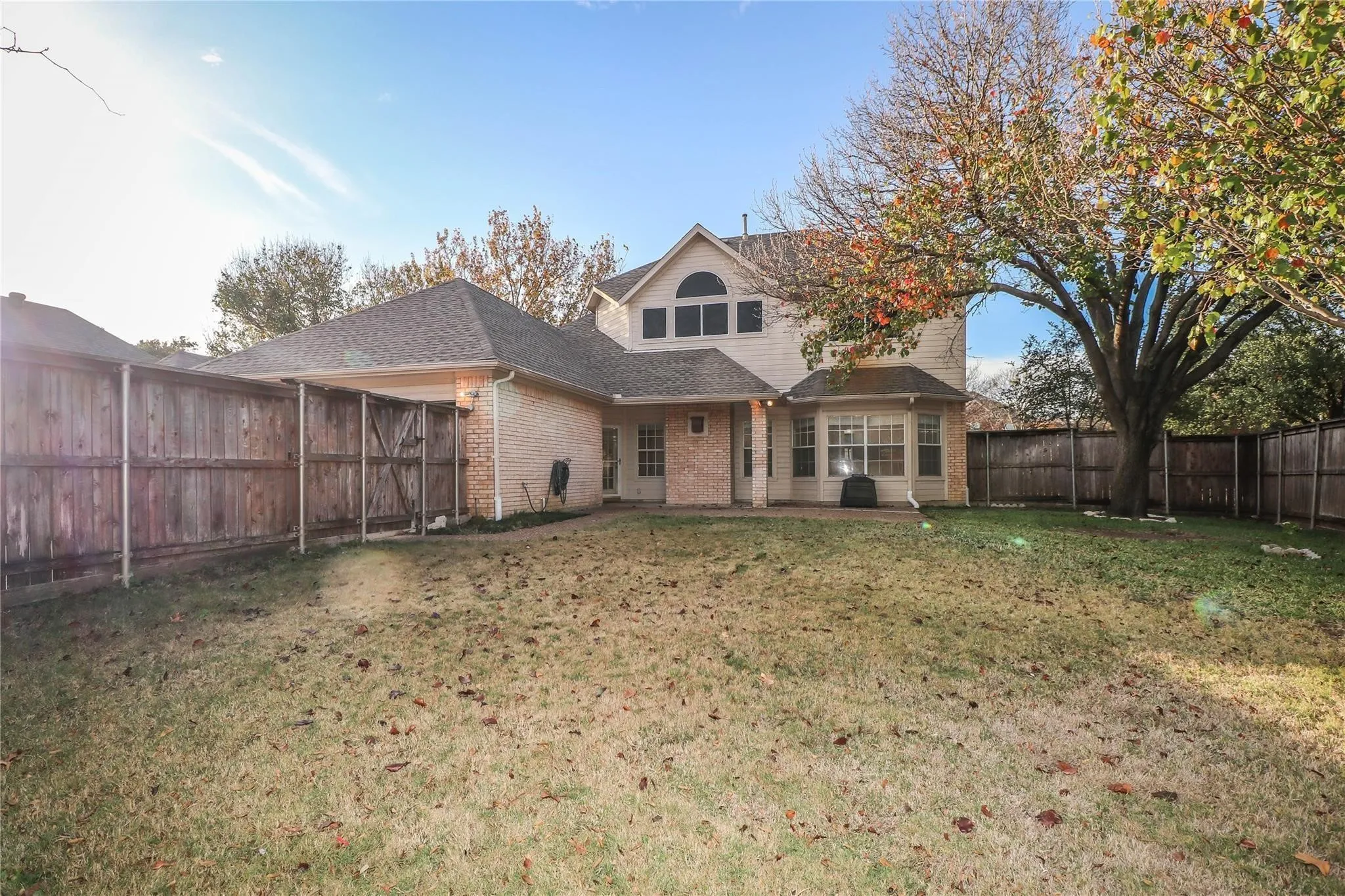 Exterior elevation featuring a brick and siding facade, a multi-gabled roofline, an arched window, and an enclosed backyard with a wood privacy fence