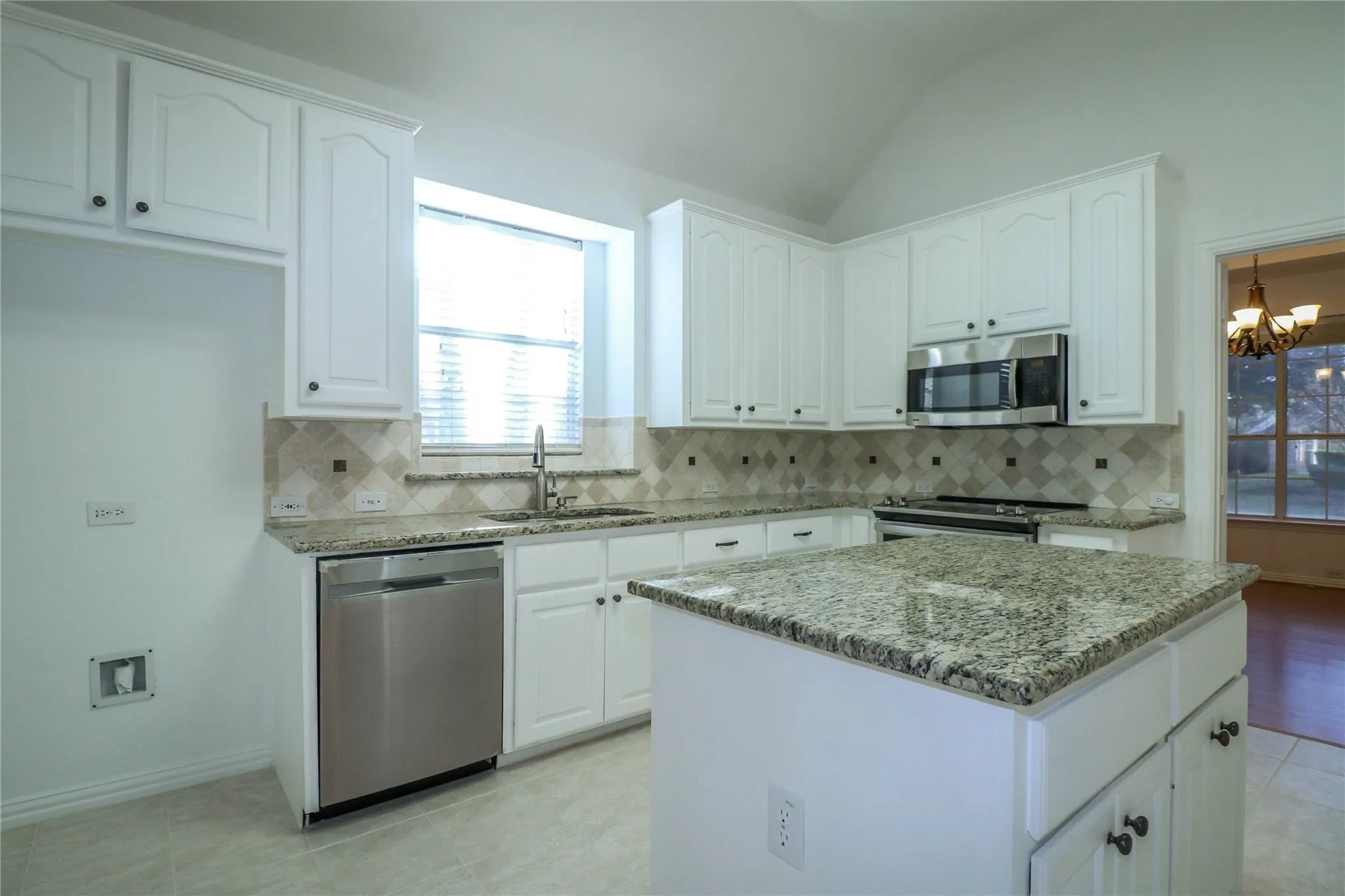 Kitchen featuring white shaker-style cabinetry, stone countertops, stainless steel appliances, a central island, and a tile backsplash with diamond-pattern accents