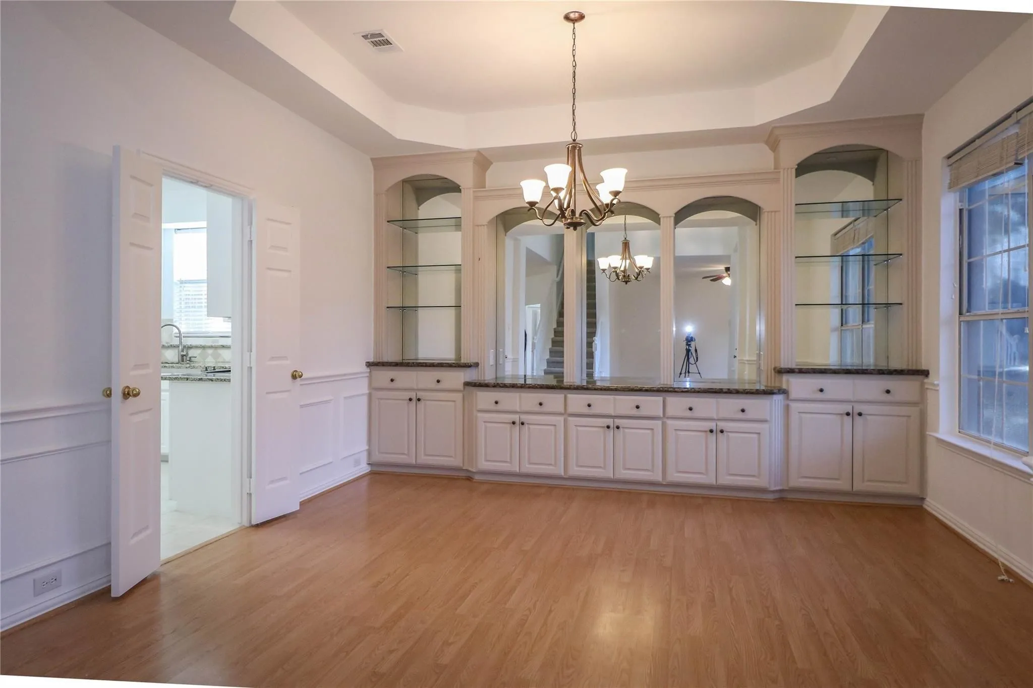Tray ceiling featuring a decorative chandelier, expansive built-in cabinetry with glass shelving, mirrored accents, and wood-finish flooring