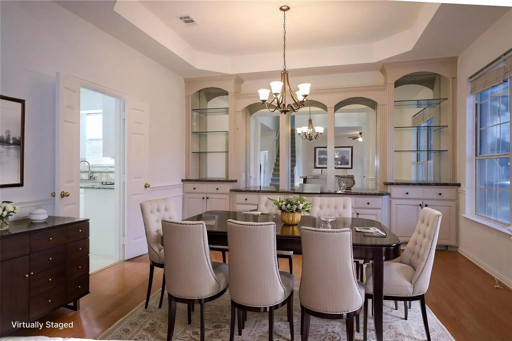 Tray ceiling with central chandelier, built-in cabinetry featuring arched glass shelving, and wood-finish flooring