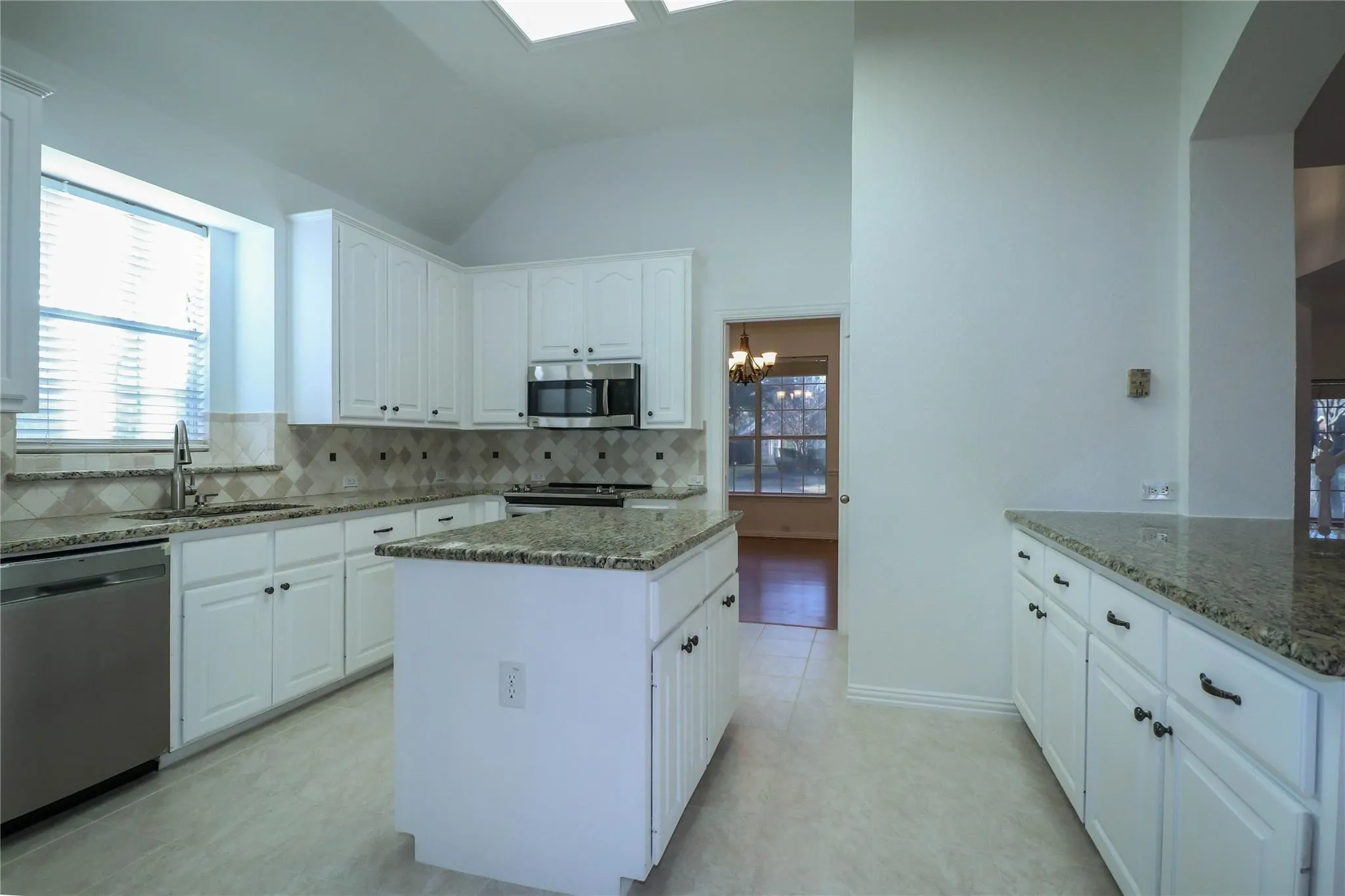 Kitchen featuring white cabinetry, stone-surface countertops, center island, tiled backsplash, and vaulted ceiling with skylights