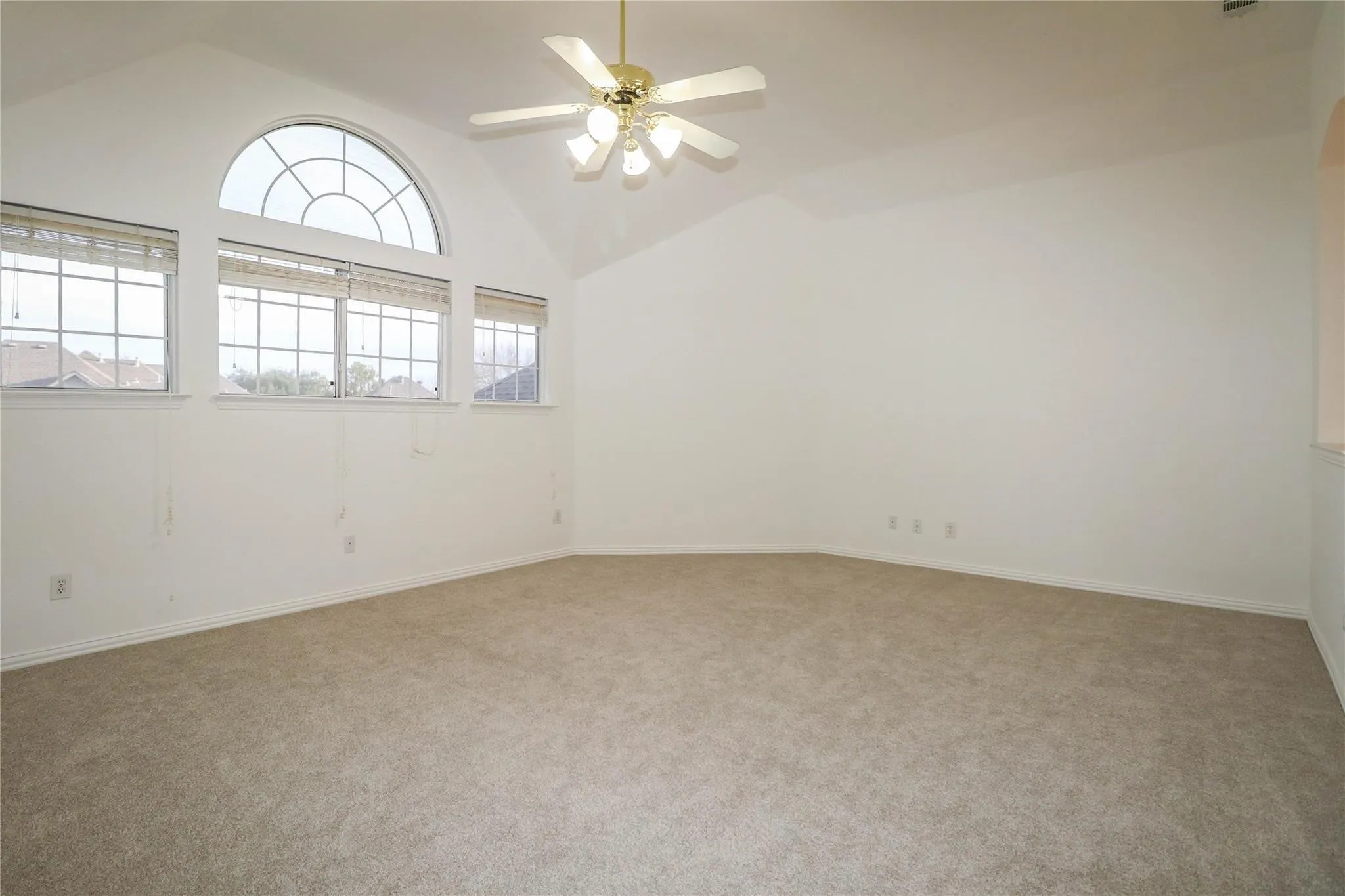 Vaulted ceiling featuring a central multi-light fan, expansive wall of grid-style windows with an arched transom, and neutral carpeting