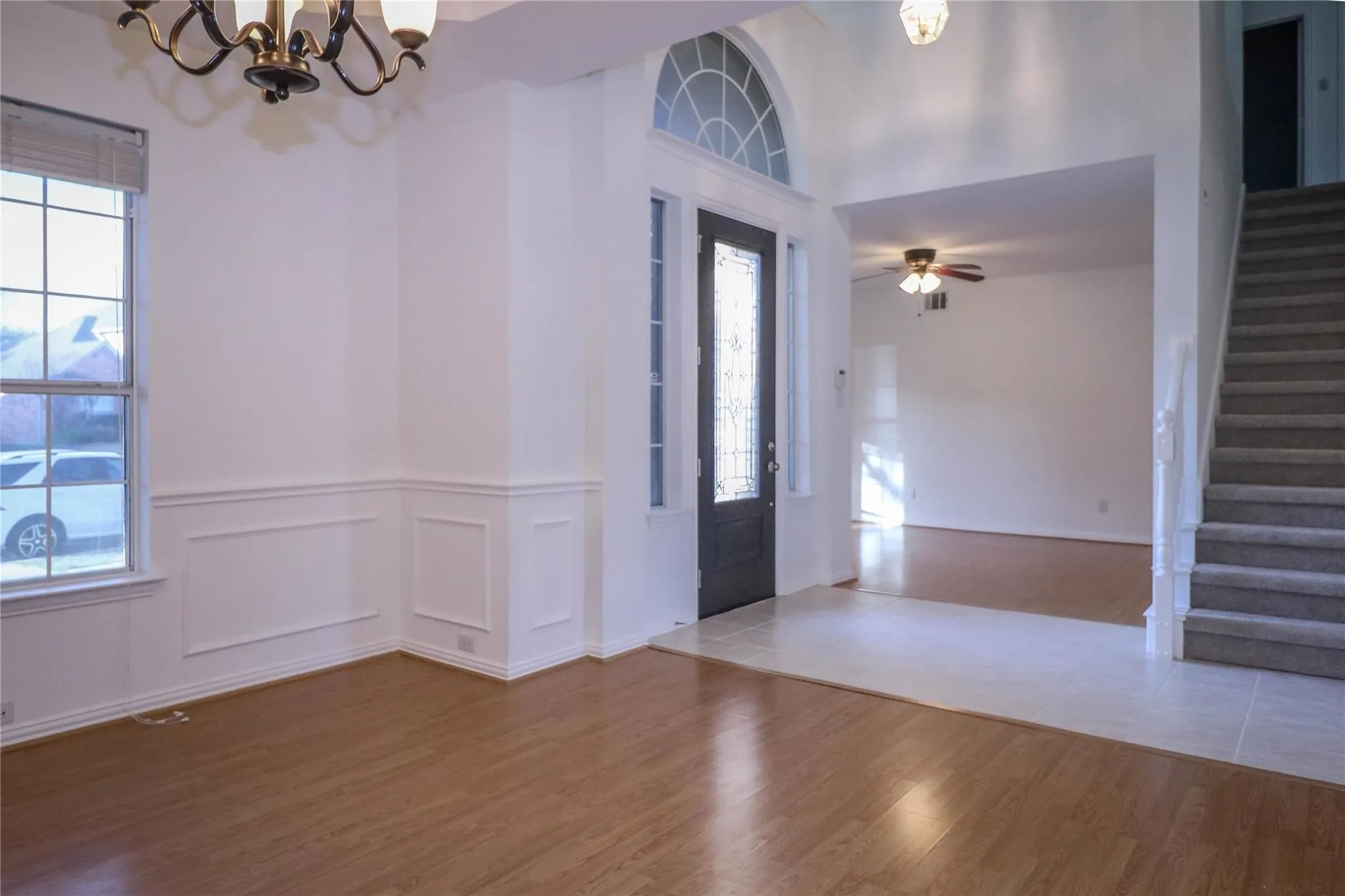 Foyer featuring a high ceiling, wainscoting, wood-finish flooring, a decorative arched transom window, and a staircase with a white balustrade