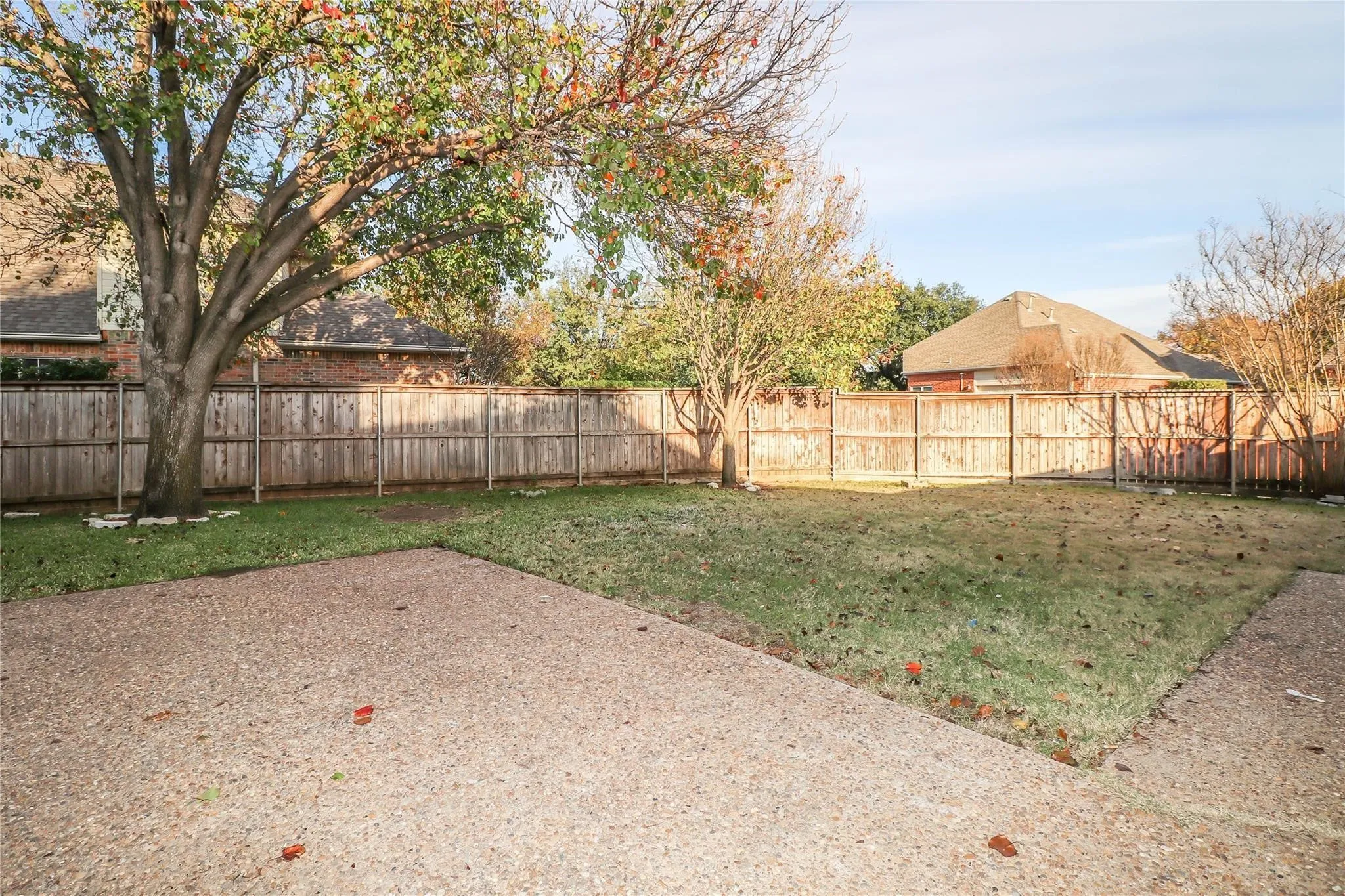 Backyard featuring a concrete patio, grass lawn, wood privacy fencing, and mature trees
