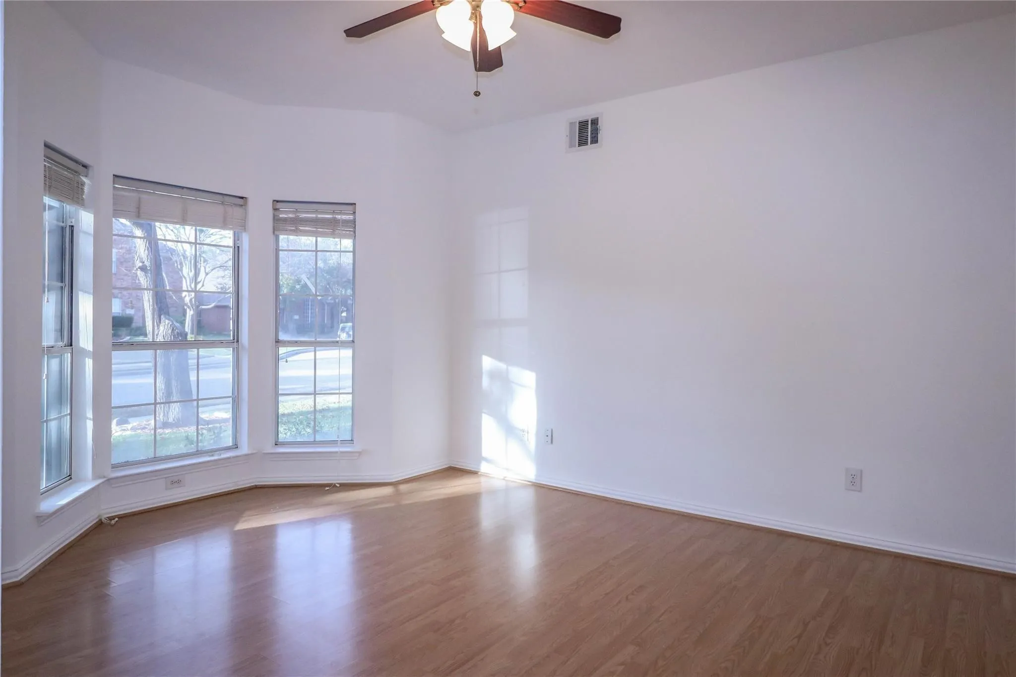 Room featuring wood-finish flooring, a bay window configuration, and an attached ceiling fan with a light fixture