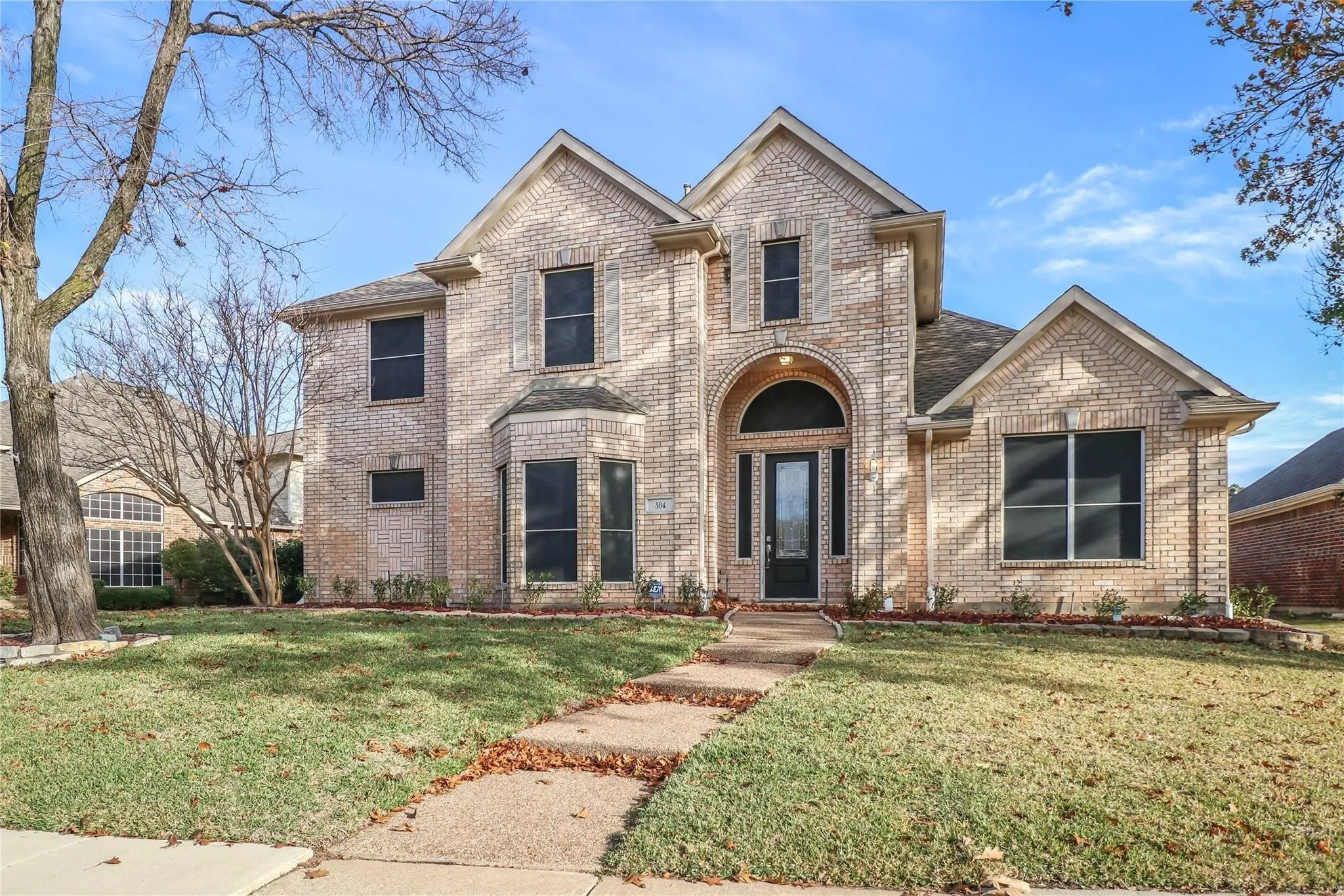 Two-story brick exterior featuring a multi-gabled roofline, an arched entryway, decorative shutters, and a covered front porch