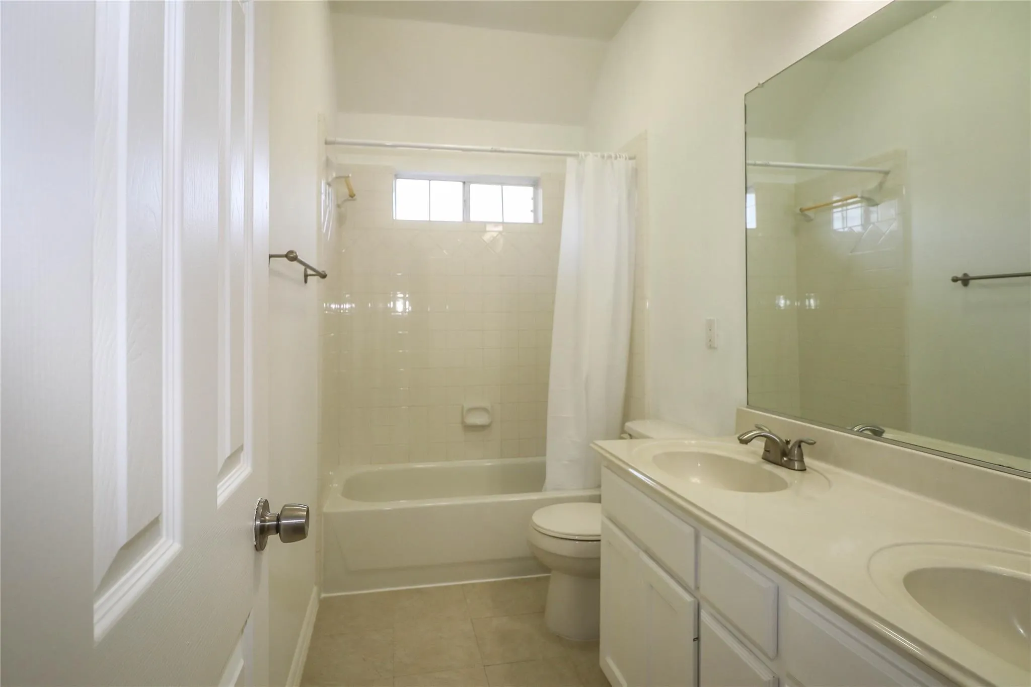 Bathroom featuring a dual-sink vanity with solid-surface countertops, a porcelain tub-and-shower combination with tile surround, and a large wall-mounted mirror