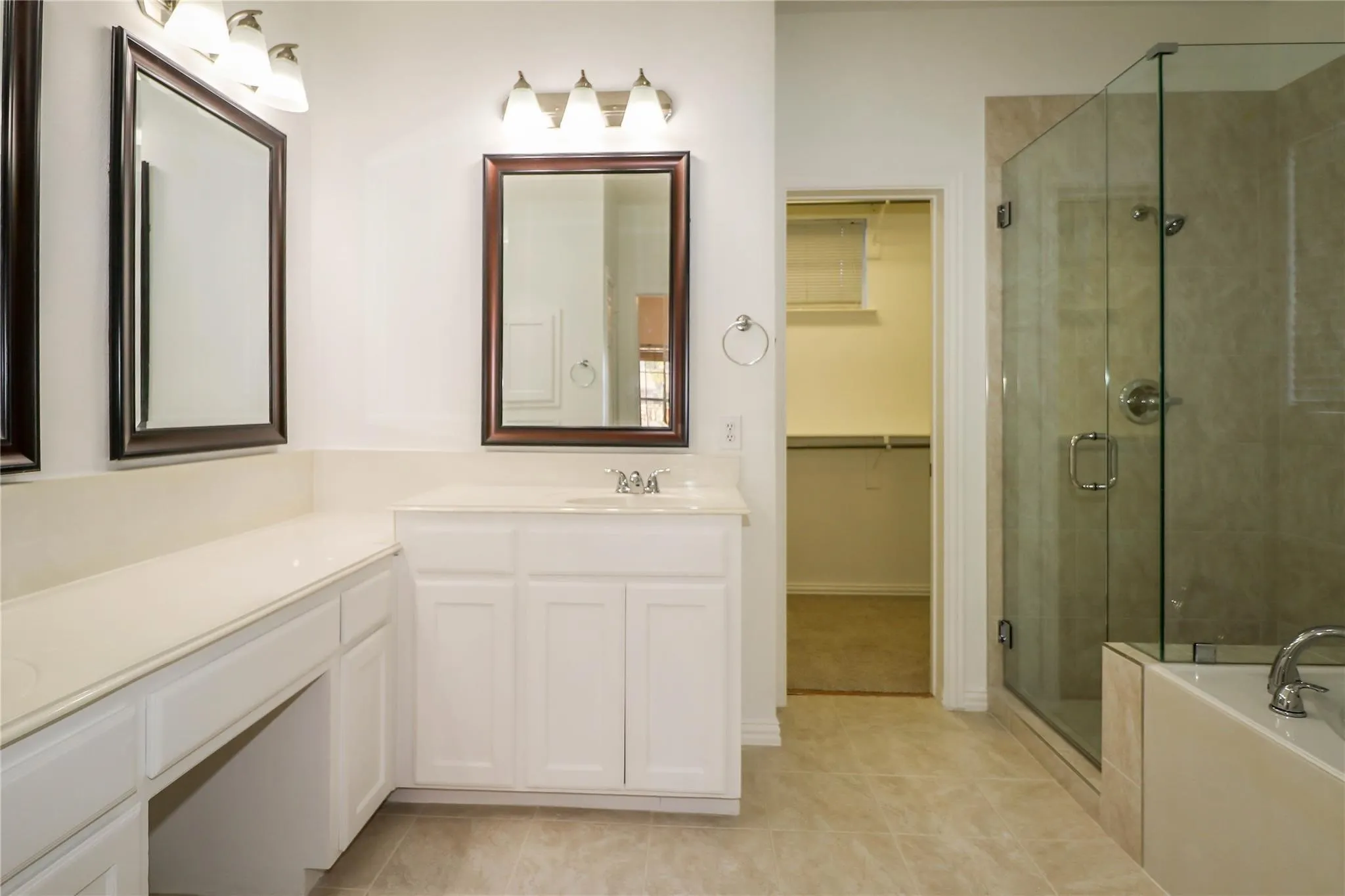 White cabinetry vanity with stone countertop, framed wall mirrors, three-light fixtures, glass-enclosed shower, and built-in closet shelving