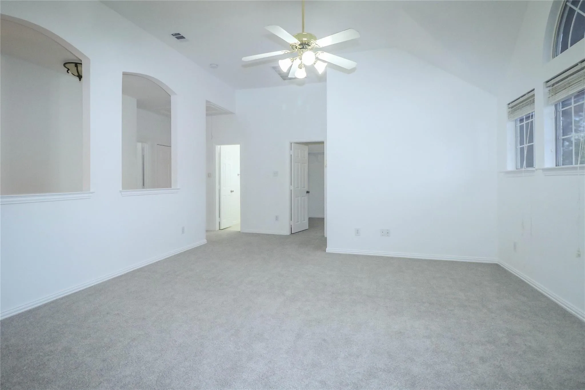Vaulted ceilings featuring recessed arch niches, carpeted flooring, and a multi-light ceiling fan