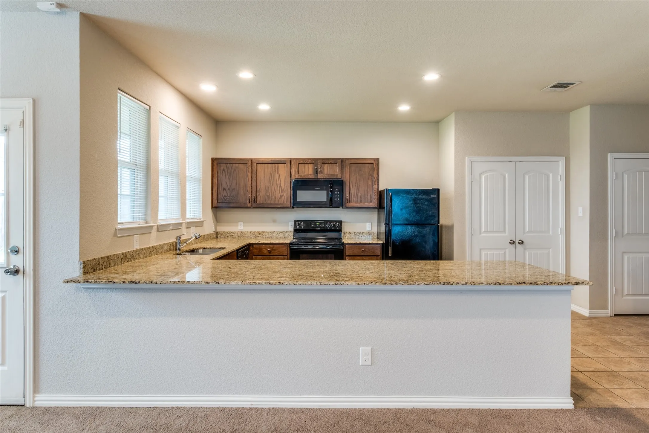 Kitchen featuring stone-finish countertops, dark wood cabinetry, recessed lighting, and a breakfast bar