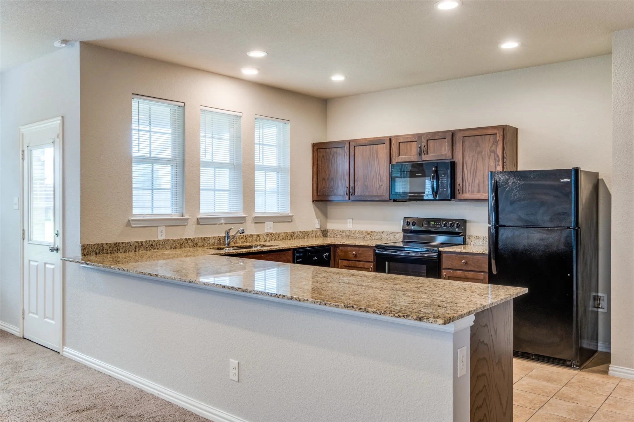 Kitchen featuring stone countertops, an expansive breakfast bar, dark wood cabinetry, recessed lighting, and a set of three windows