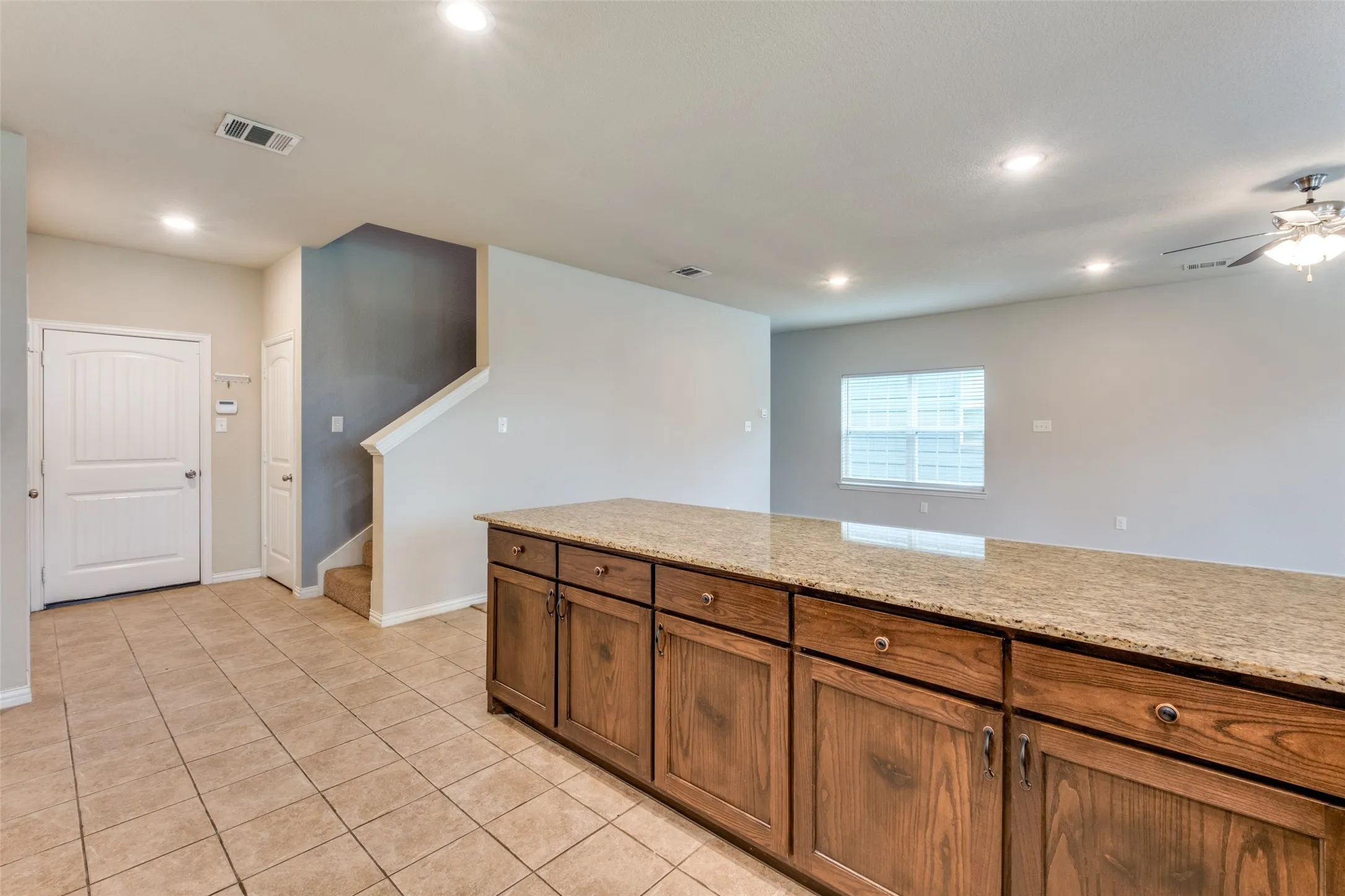 Kitchen island with stone countertop and wood-finish cabinetry, tile flooring, recessed lighting, and ceiling fan