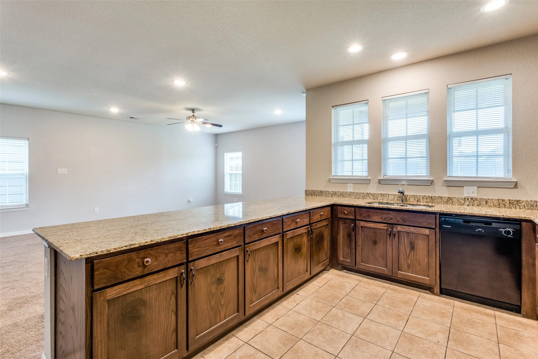 Kitchen featuring wood cabinetry, stone-finish countertops, tile flooring, recessed lighting, and a built-in dishwasher