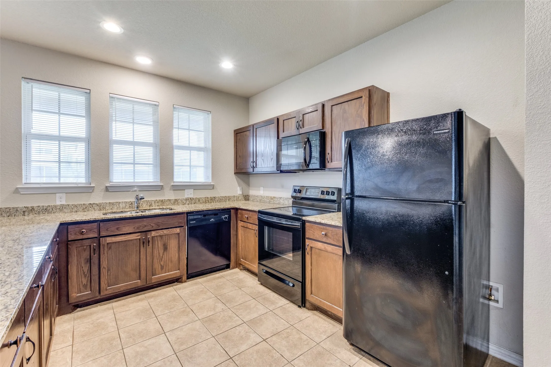 Kitchen featuring wooden cabinetry, stone-surface countertops, tile flooring, recessed lighting, and black appliances