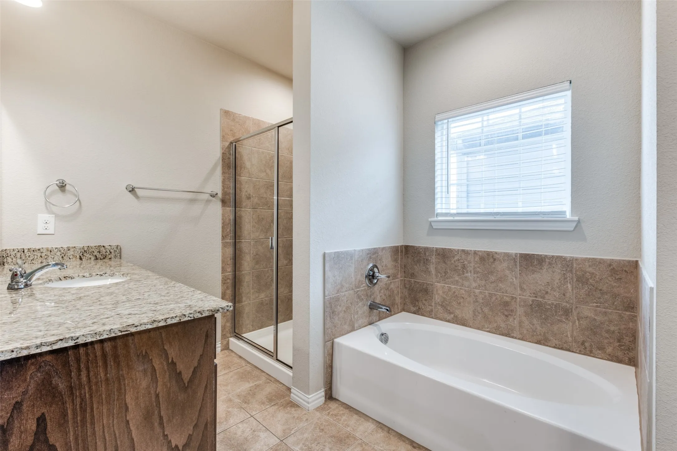 Bathroom featuring a granite countertop vanity, a tiled walk-in shower with a glass enclosure, a deep soaking tub with a tiled surround, and a window with blinds