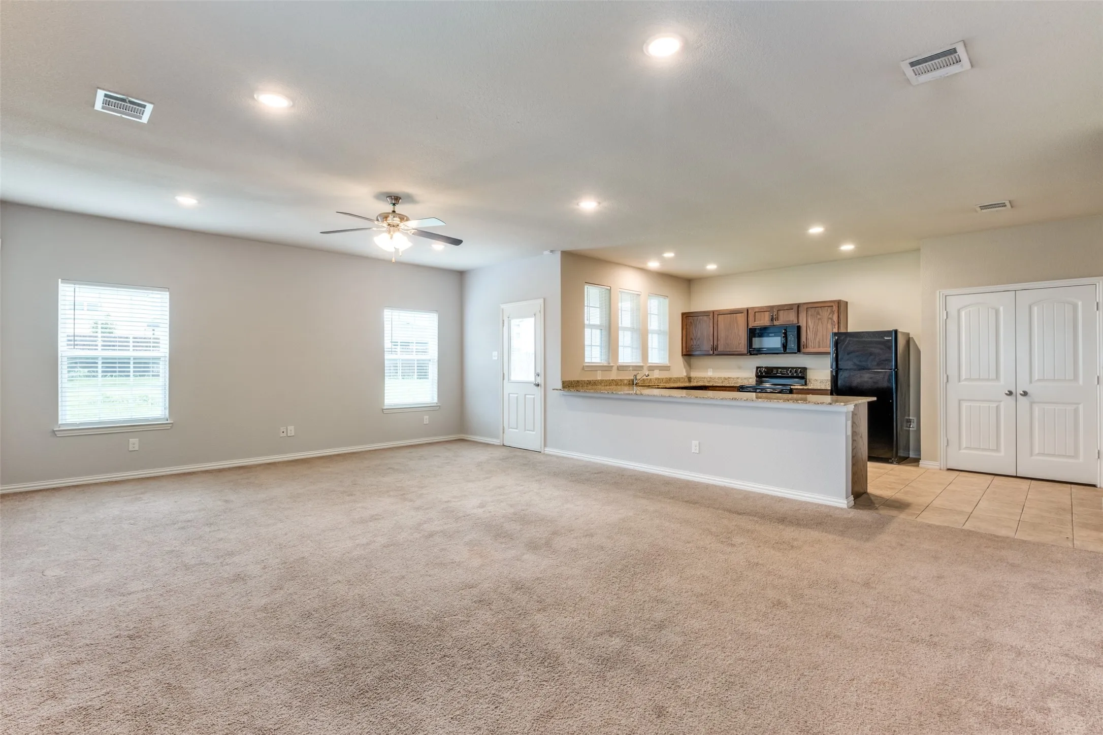 Open-concept interior featuring recessed lighting, a ceiling fan, stone-surfaced breakfast bar, wood-finish cabinetry, and neutral carpeting
