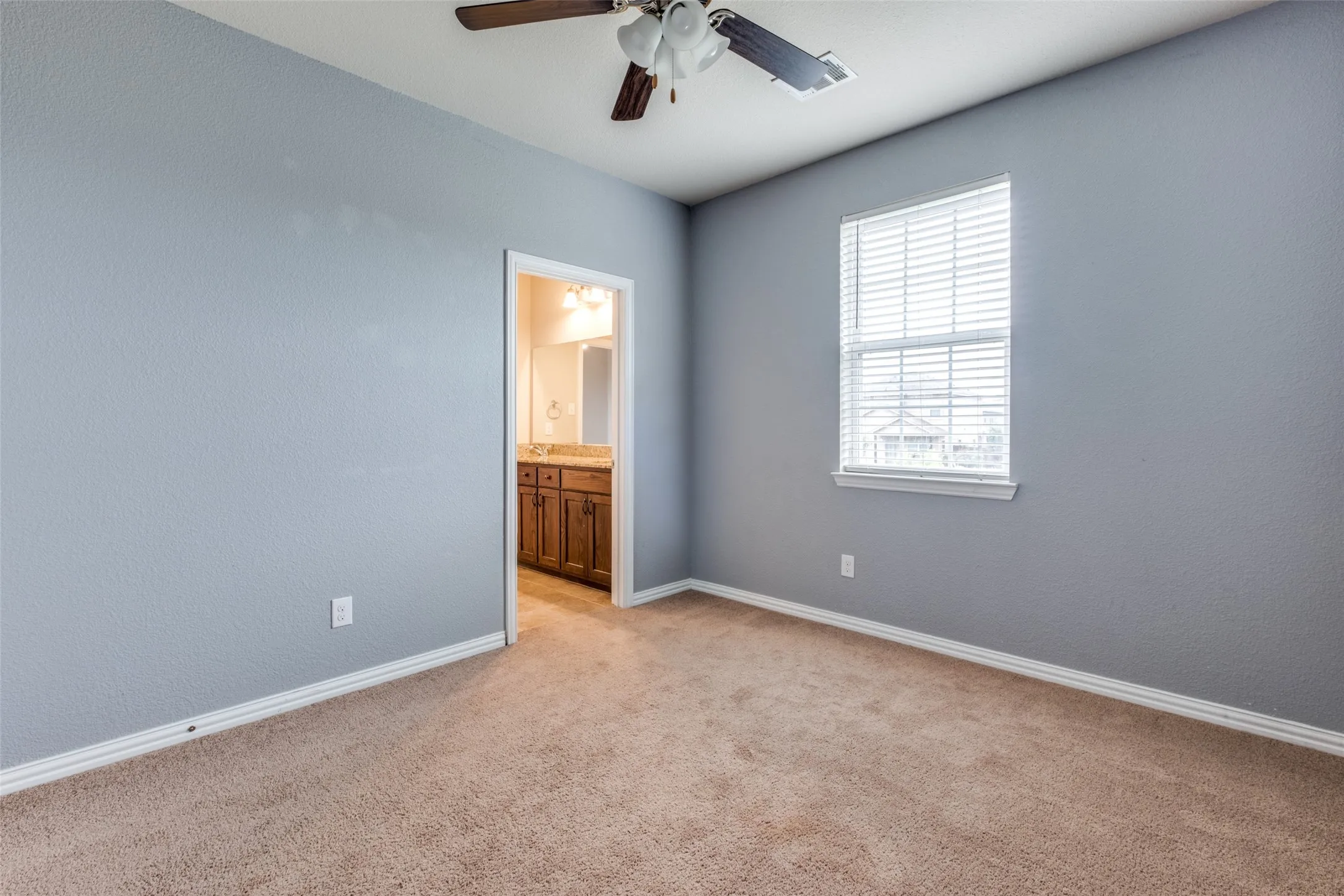 Neutral wall tones paired with neutral carpeting, single-hung window with adjustable blinds, and ceiling fan with integrated lighting