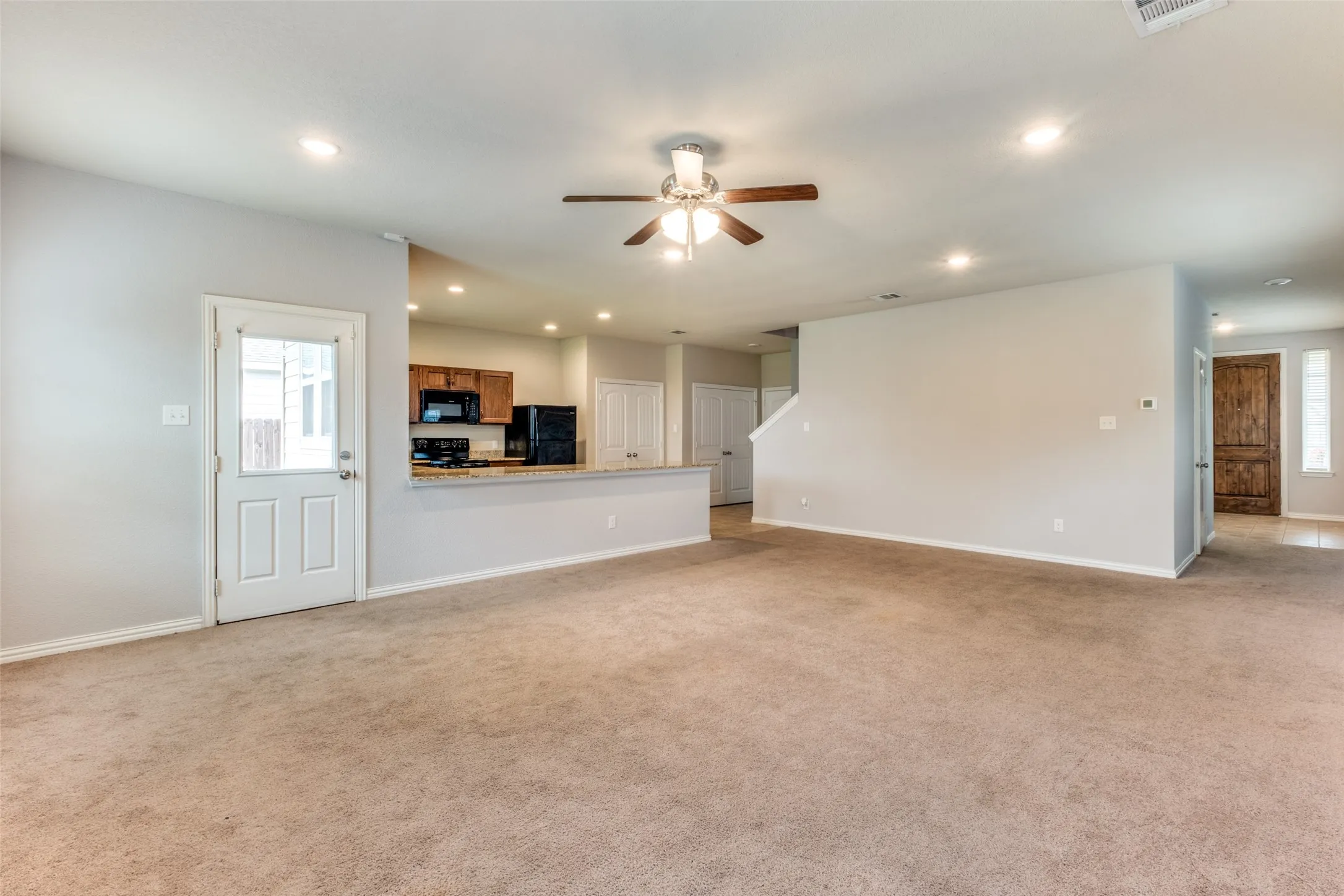 Open-concept interior featuring carpeting, a ceiling fan with integrated lighting, recessed lighting, a pass-through kitchen counter, and a single-light door