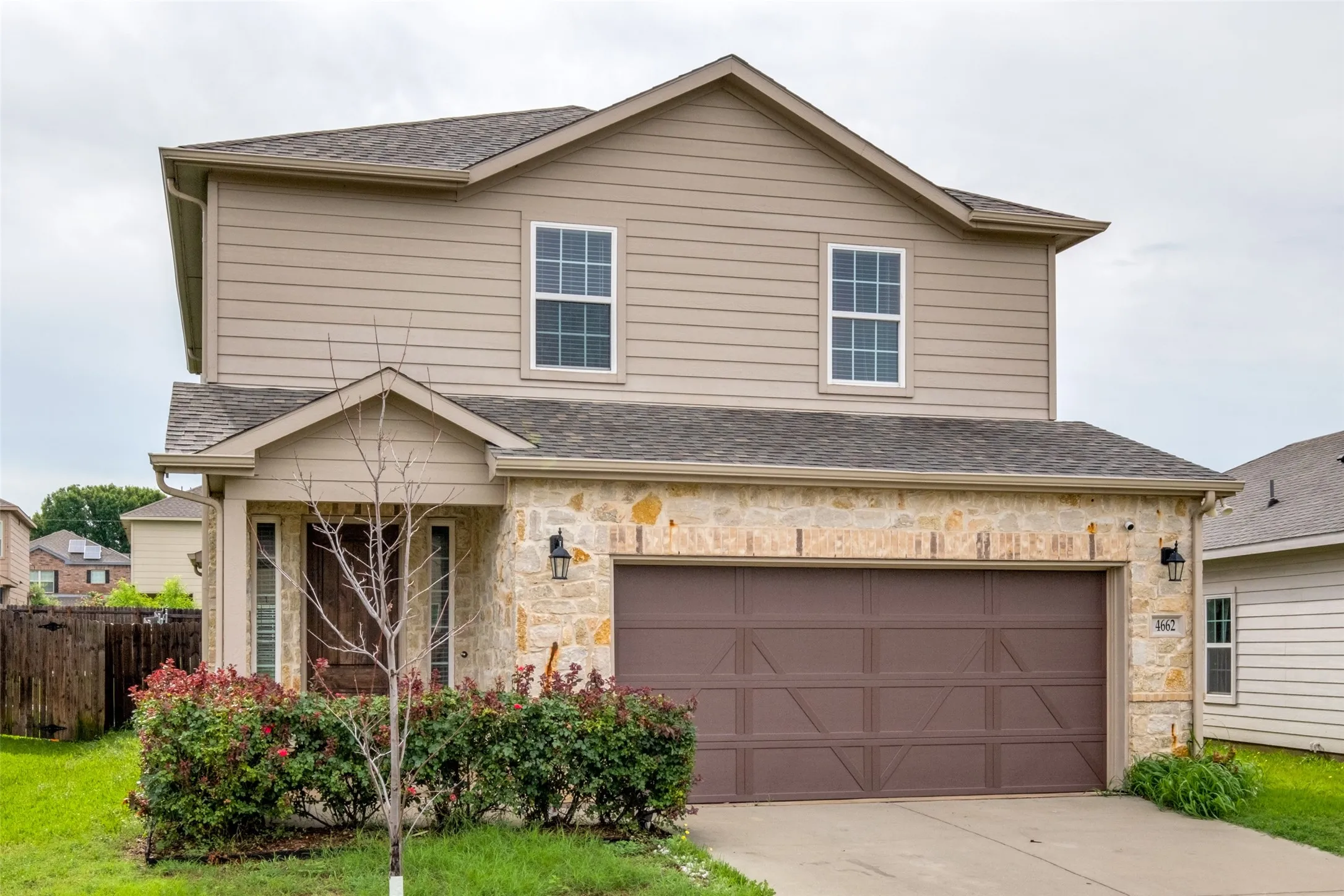 Two-story exterior featuring a mix of horizontal lap siding and decorative stone masonry, a shingled roof, attached two-car garage, and a covered front entry