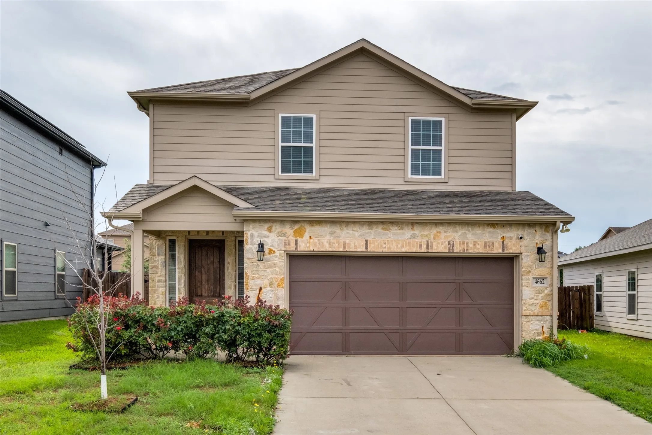 Two-story residence featuring a partial stone facade, horizontal siding, a covered entryway, and an attached two-car garage with cross-buck detailing