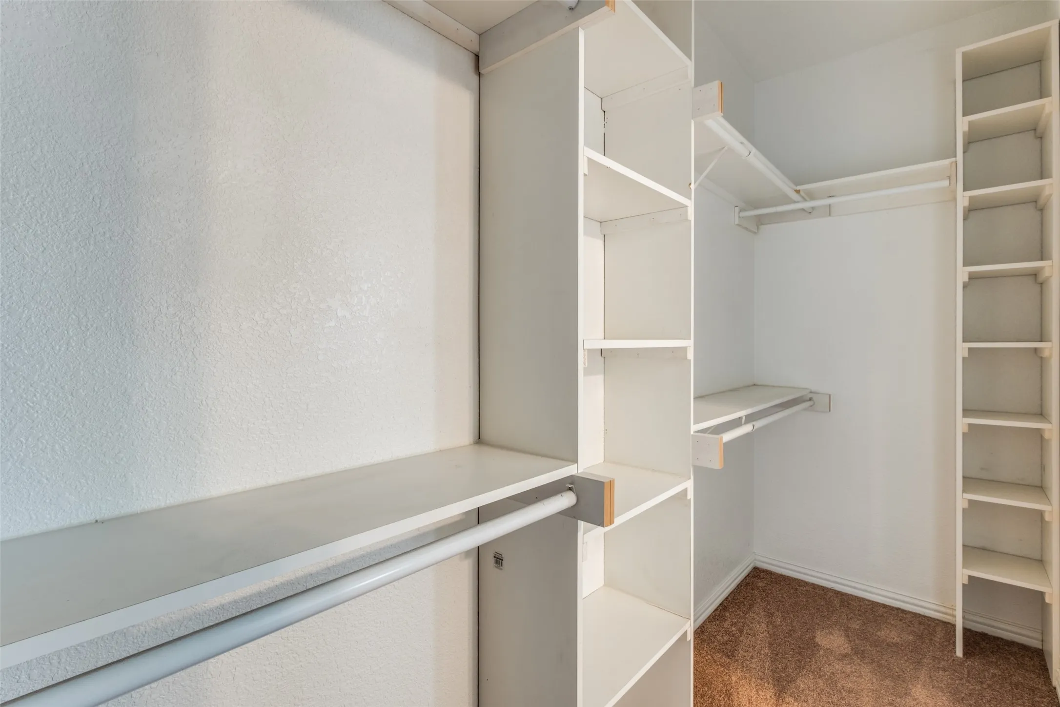 Walk-in closet featuring white built-in shelving towers, dual-level hanging rods, and carpeting