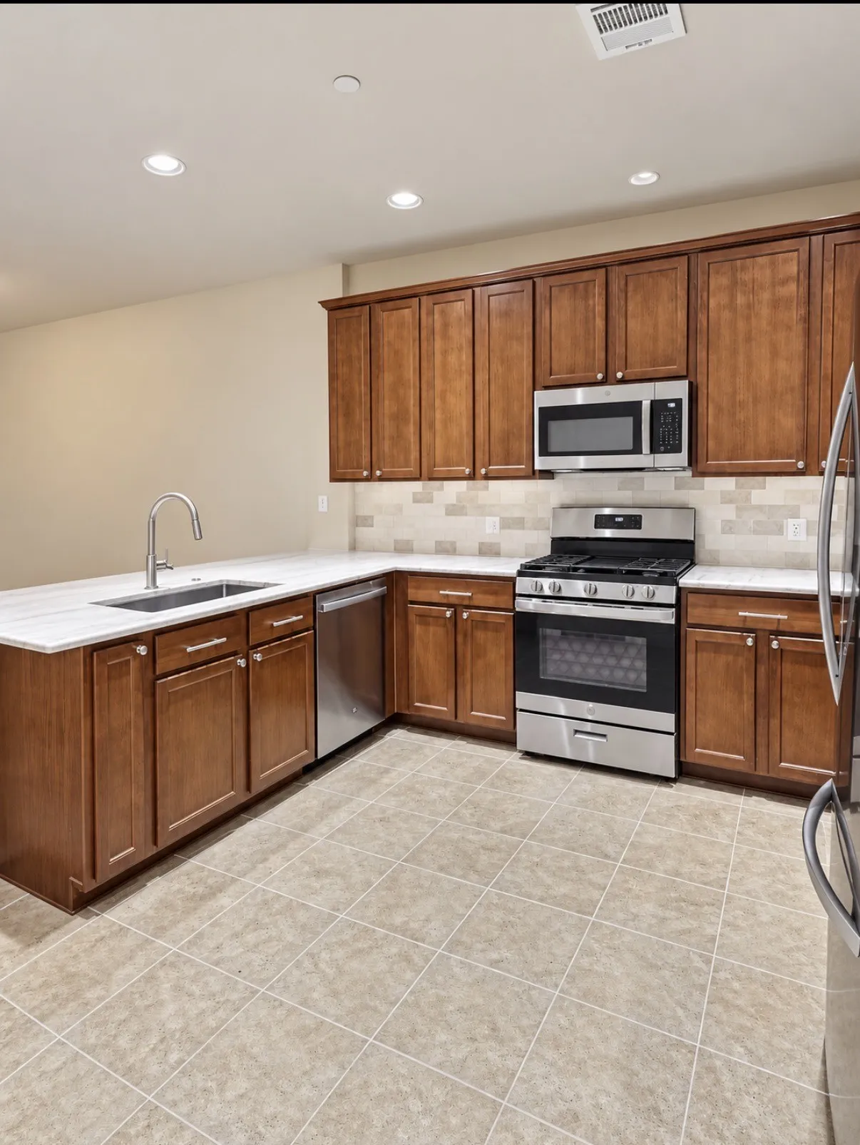 Kitchen featuring shaker-style wood cabinetry, stainless steel appliances, light-toned stone-finish countertops, tiled backsplash, and recessed lighting