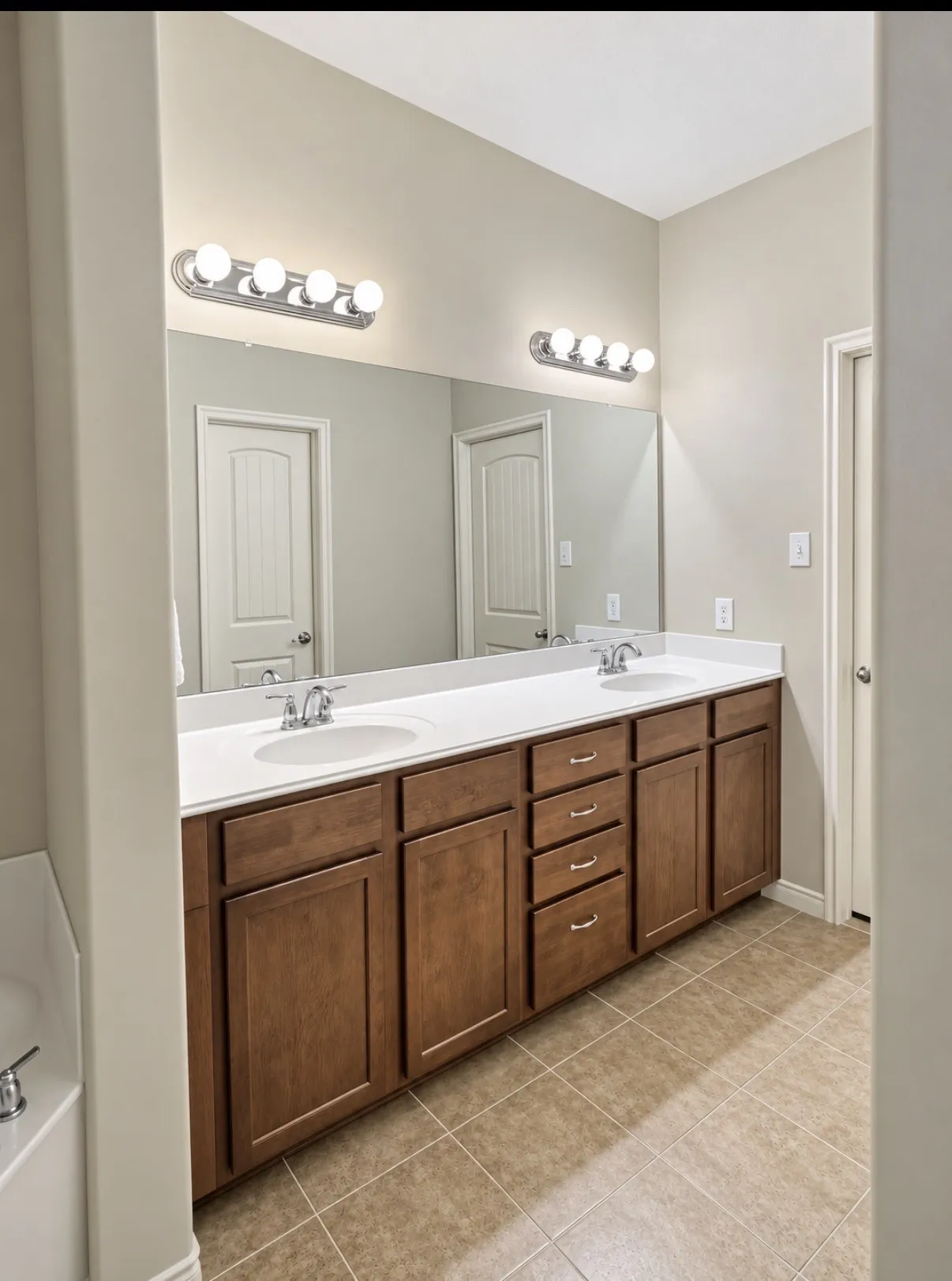 Double vanity featuring stained wood cabinetry, a solid-surface countertop, dual drop-in sinks, polished chrome faucets, and full-width wall mirror with integrated vanity lighting