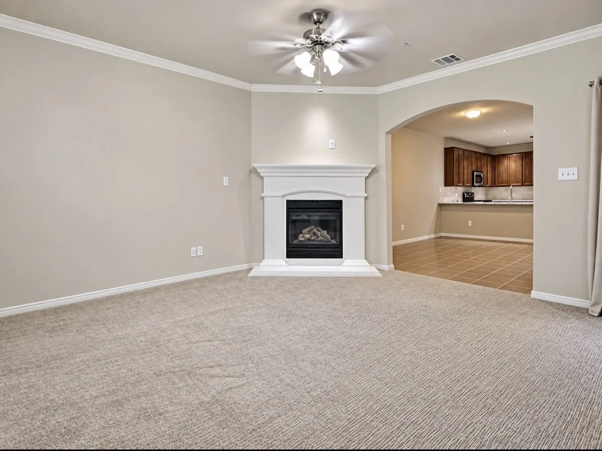Living area featuring crown molding, a central fireplace with a white mantel, an arched entry, and a ceiling fan with integrated lighting