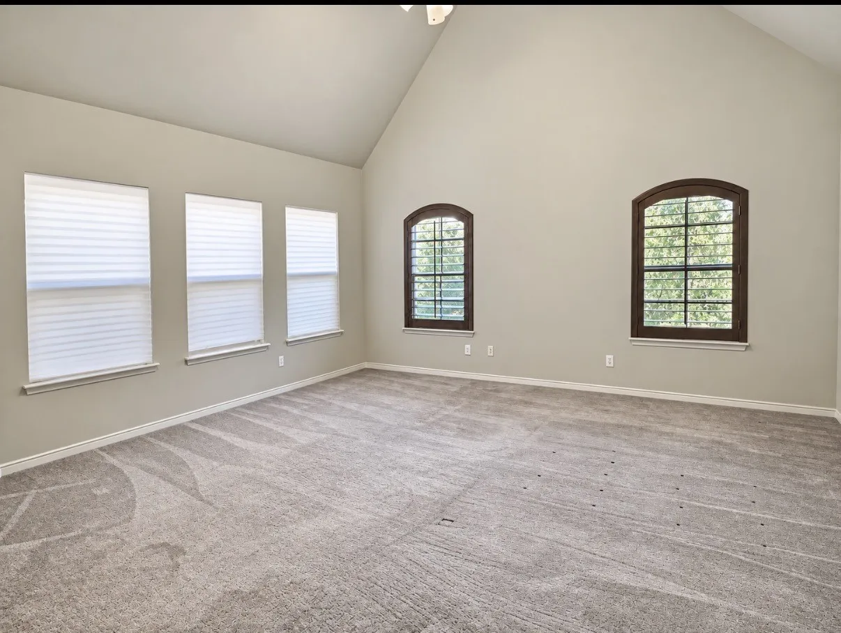 Vaulted ceiling and neutral wall tones complemented by arched windows with dark-finish frames and three rectangular windows with integrated blinds